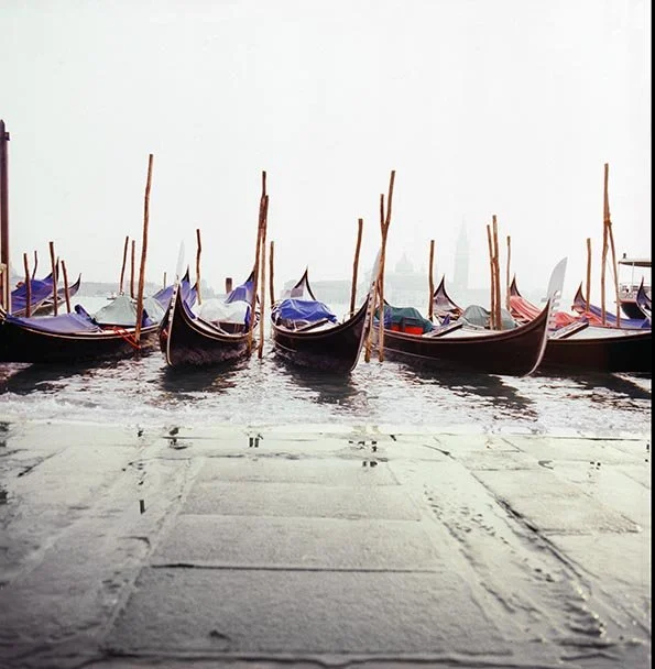 Several gondolas docked at a waterfront with water and a foggy or hazy background.