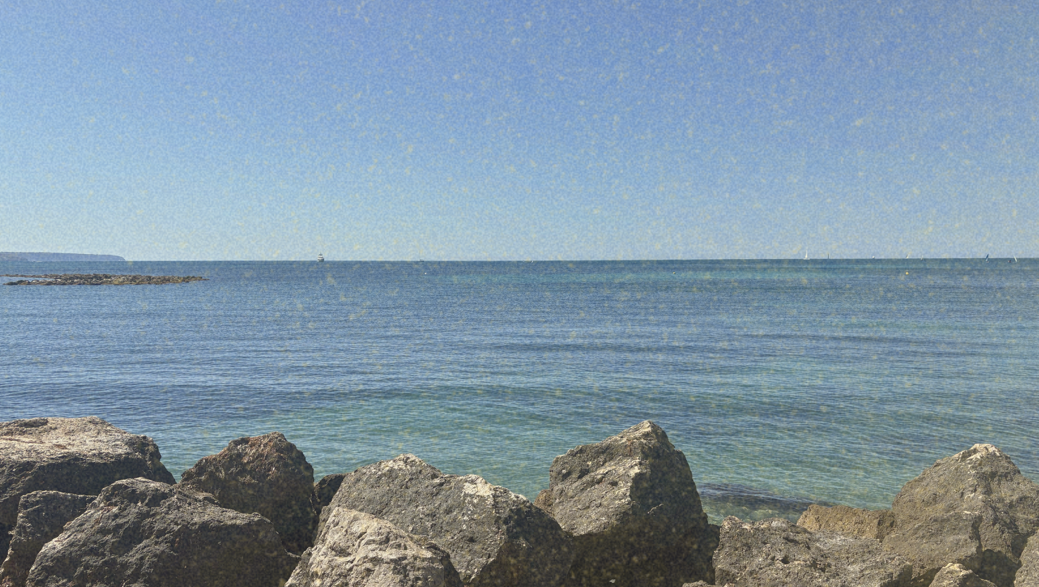 Rocky shoreline overlooking a calm ocean with clear blue sky.