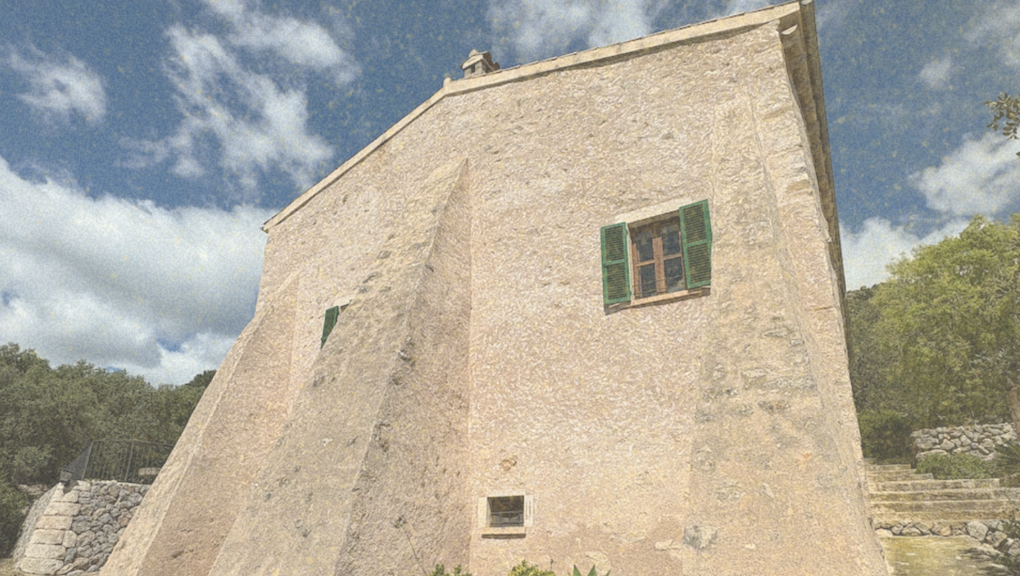 Vintage stone building with green shuttered windows, surrounded by trees and a blue sky with clouds.