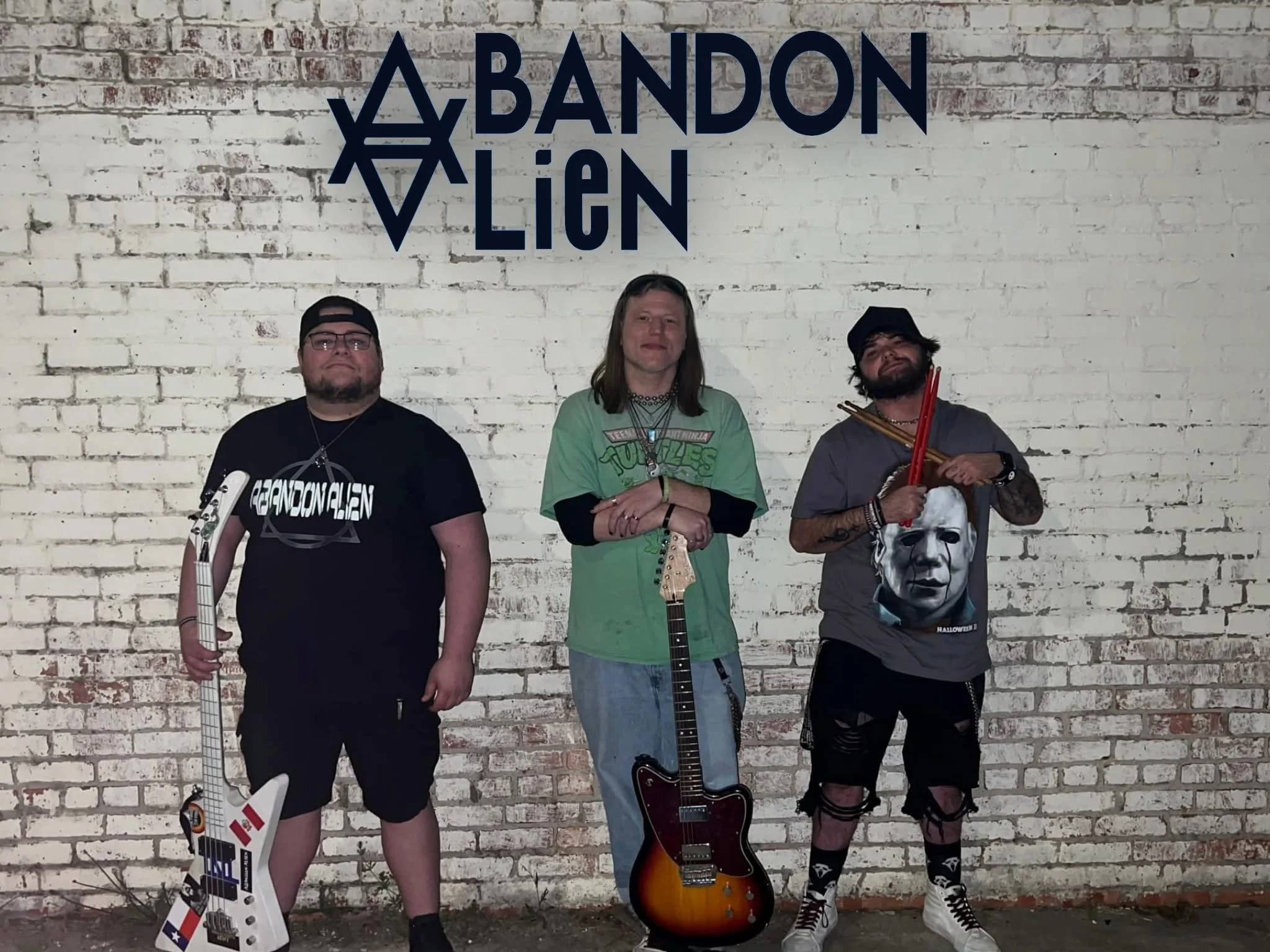 Three men standing in front of a white brick wall with a blue logo reading 'ABANDON LIEN', the man on the left is holding a white electric guitar, the man in the middle is holding an electric guitar, and the man on the right is holding drumsticks.