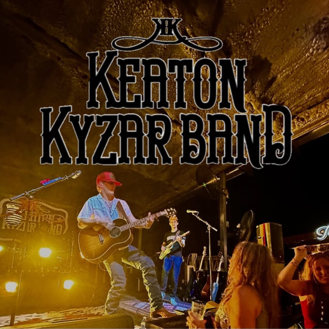 Live music performance at a venue with two musicians, one playing guitar and wearing a red cap, the other playing bass. Audience members are visible, one raising an arm. Stage lighting is warm and colorful.