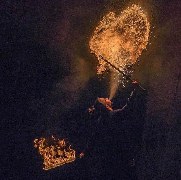 Fire performer blowing flames into the air creating a heart shape.