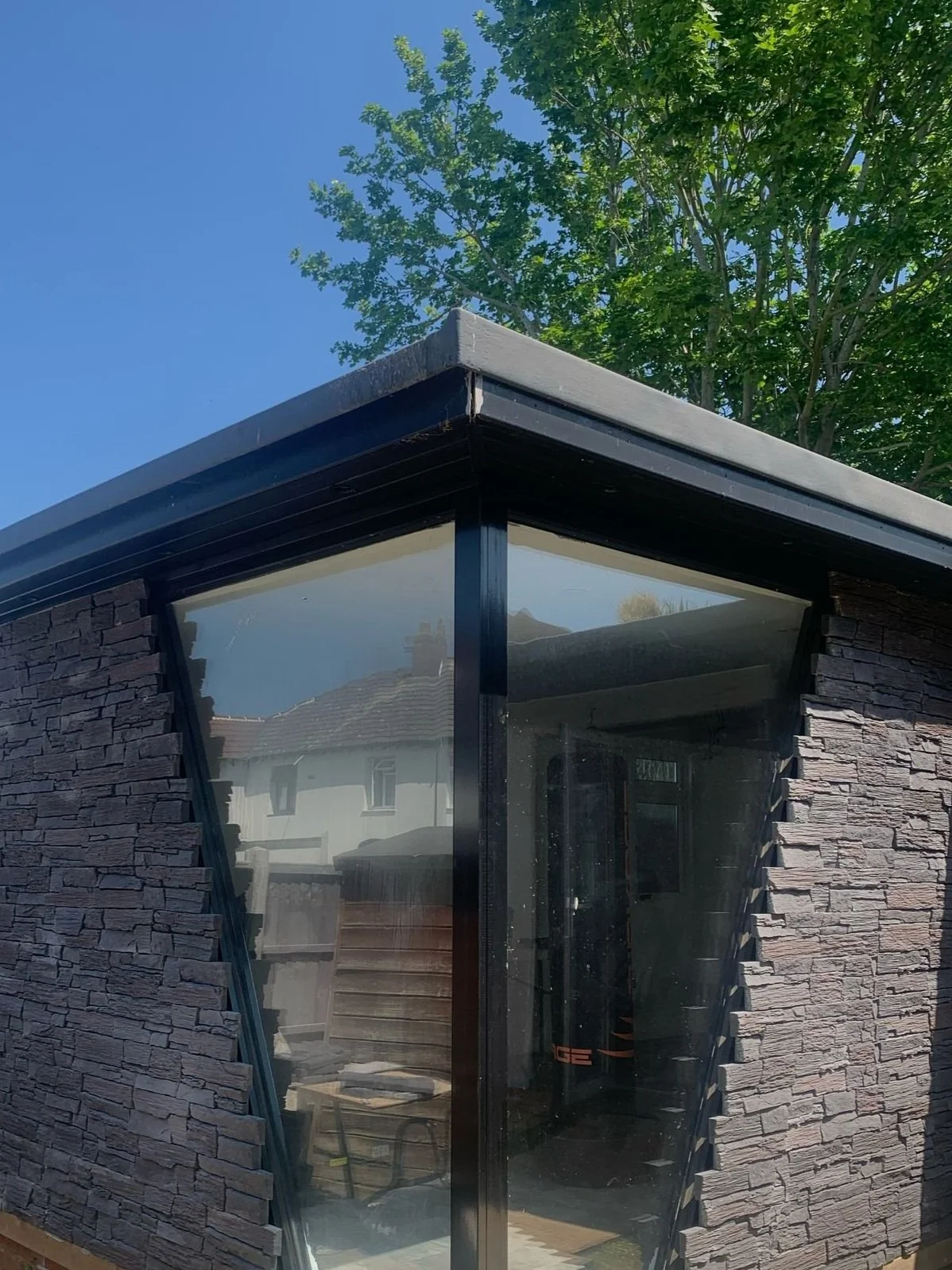 Corner of a modern building with stone cladding and large bespoke glass windows.