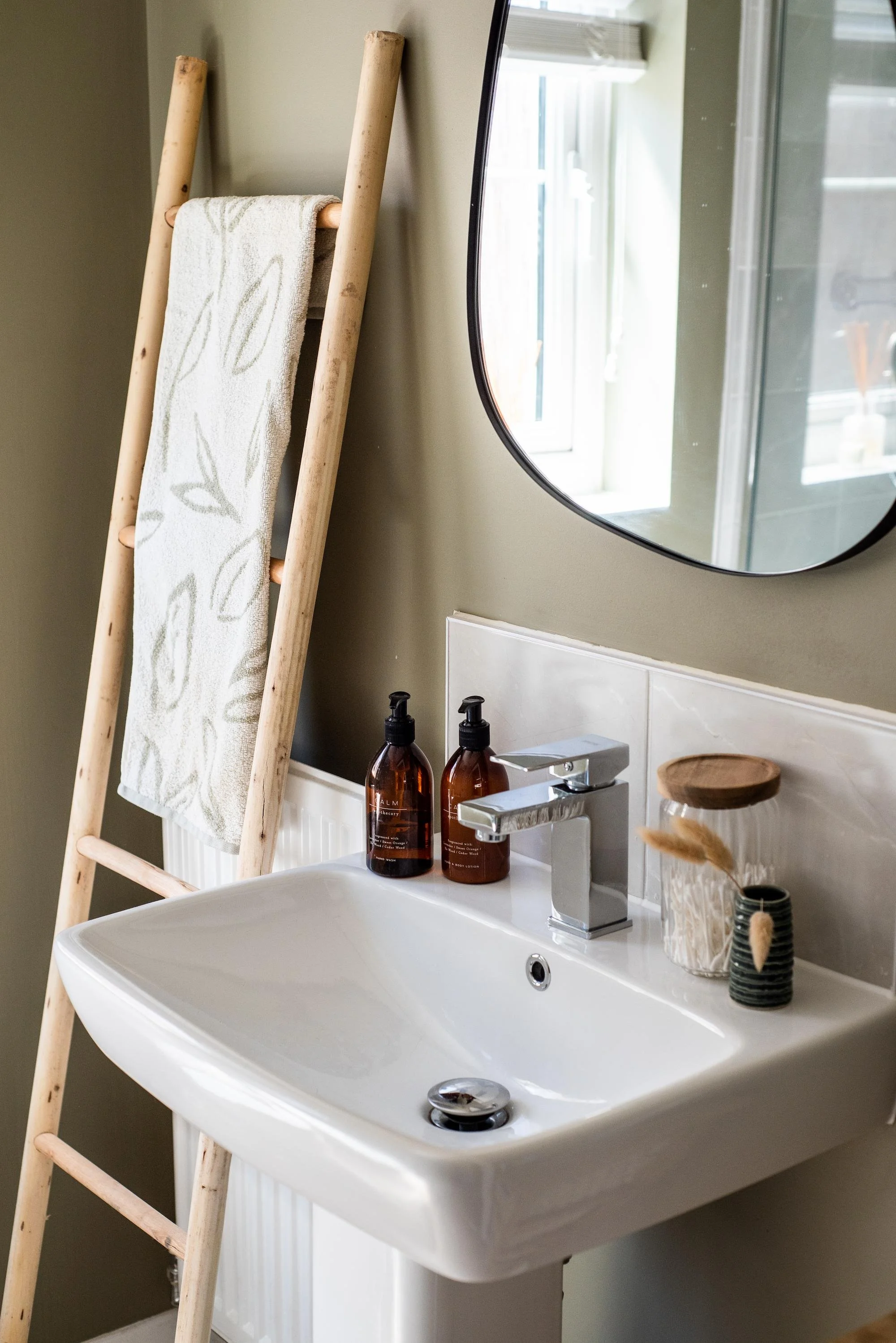 Mossy green en-suite with wooden towel ladder, pebble mirror and bathroom accessories.