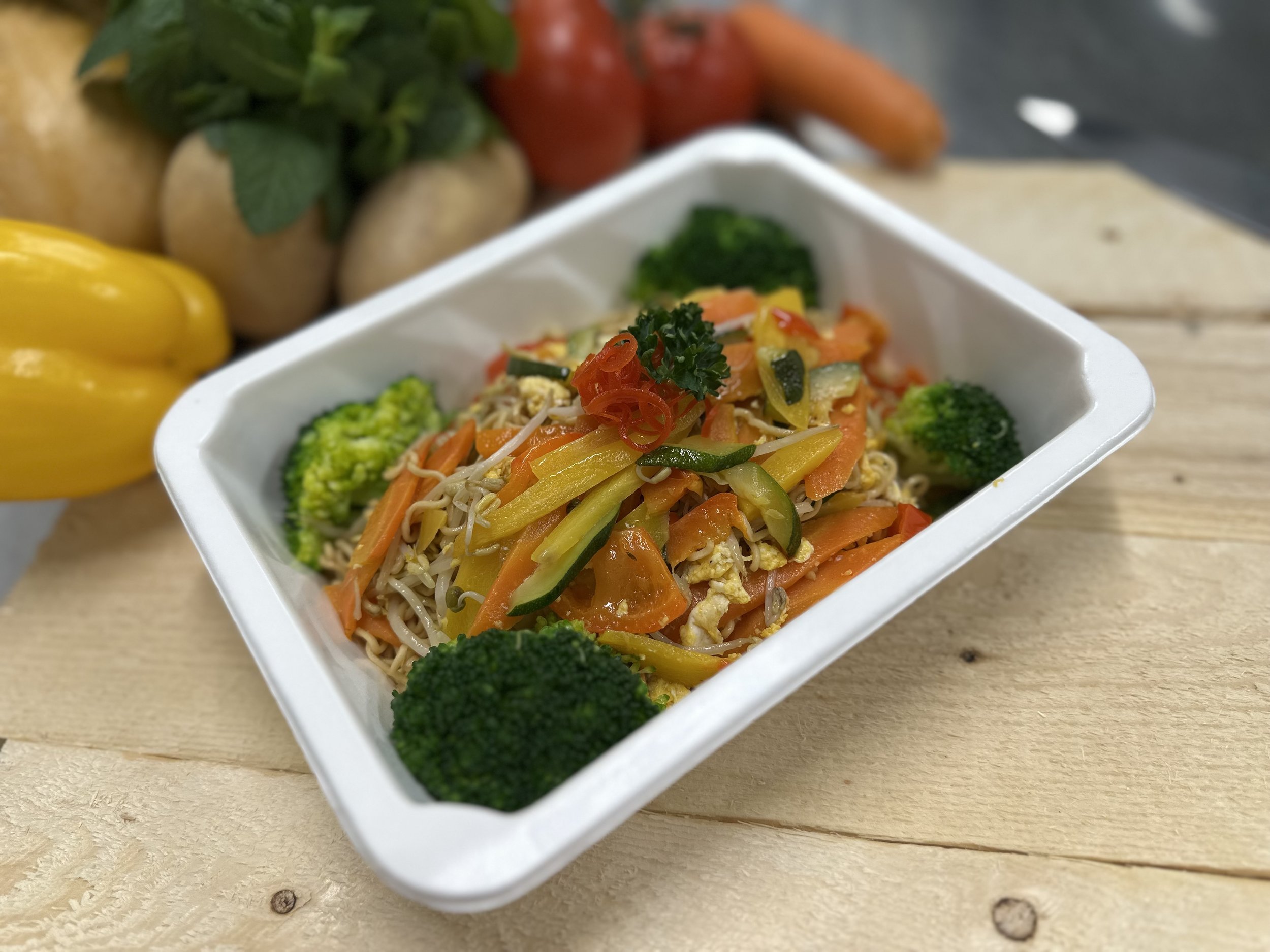 Gemüsepfanne mit Brokkoli, Karotten, Zucchini, Paprika und Noodles in einer weißen Schale