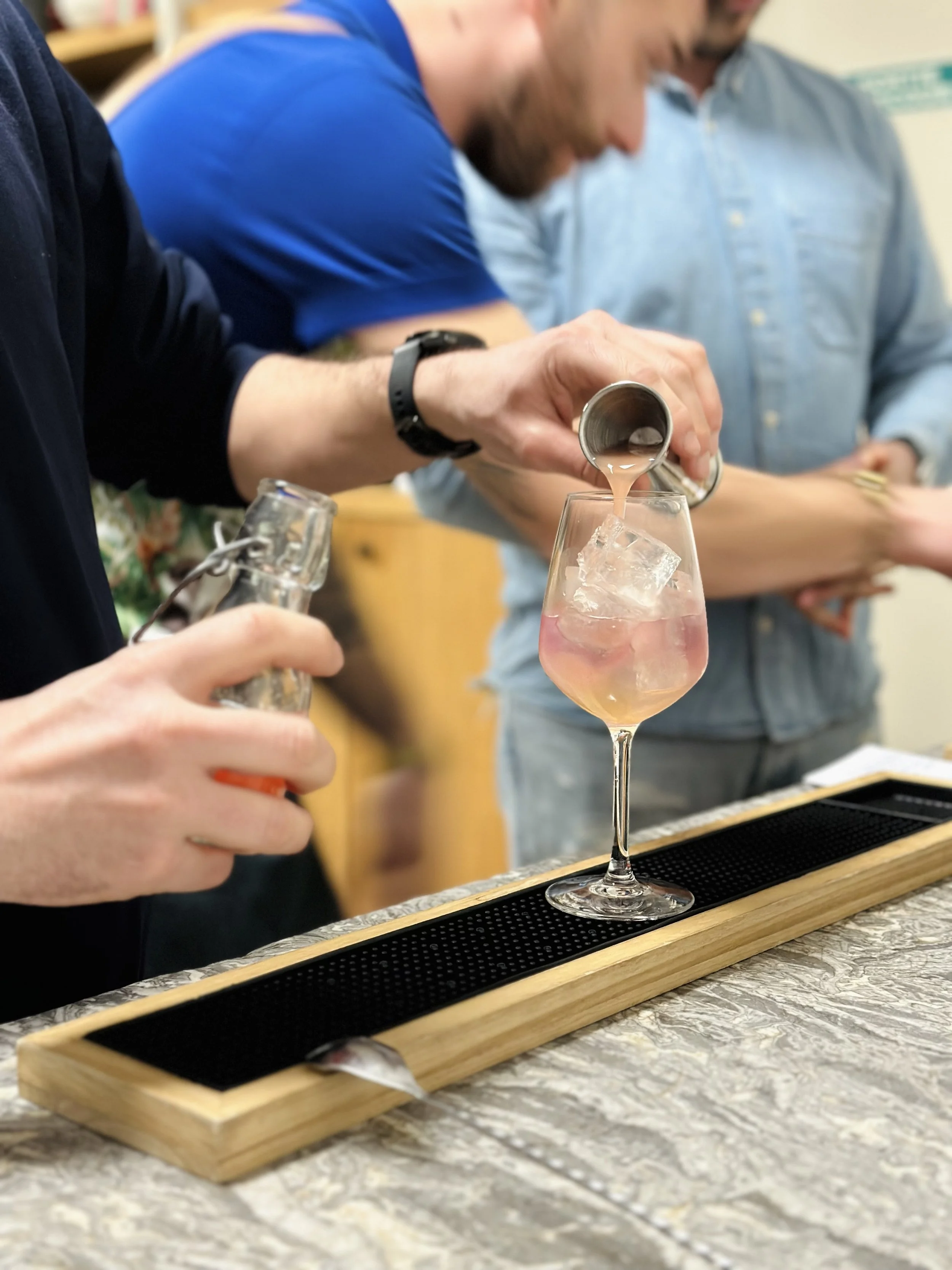 Une personne verse un cocktail rosé avec de la glace dans un verre en forme de coupe à vin, lors d'une dégustation ou d'un événement social.