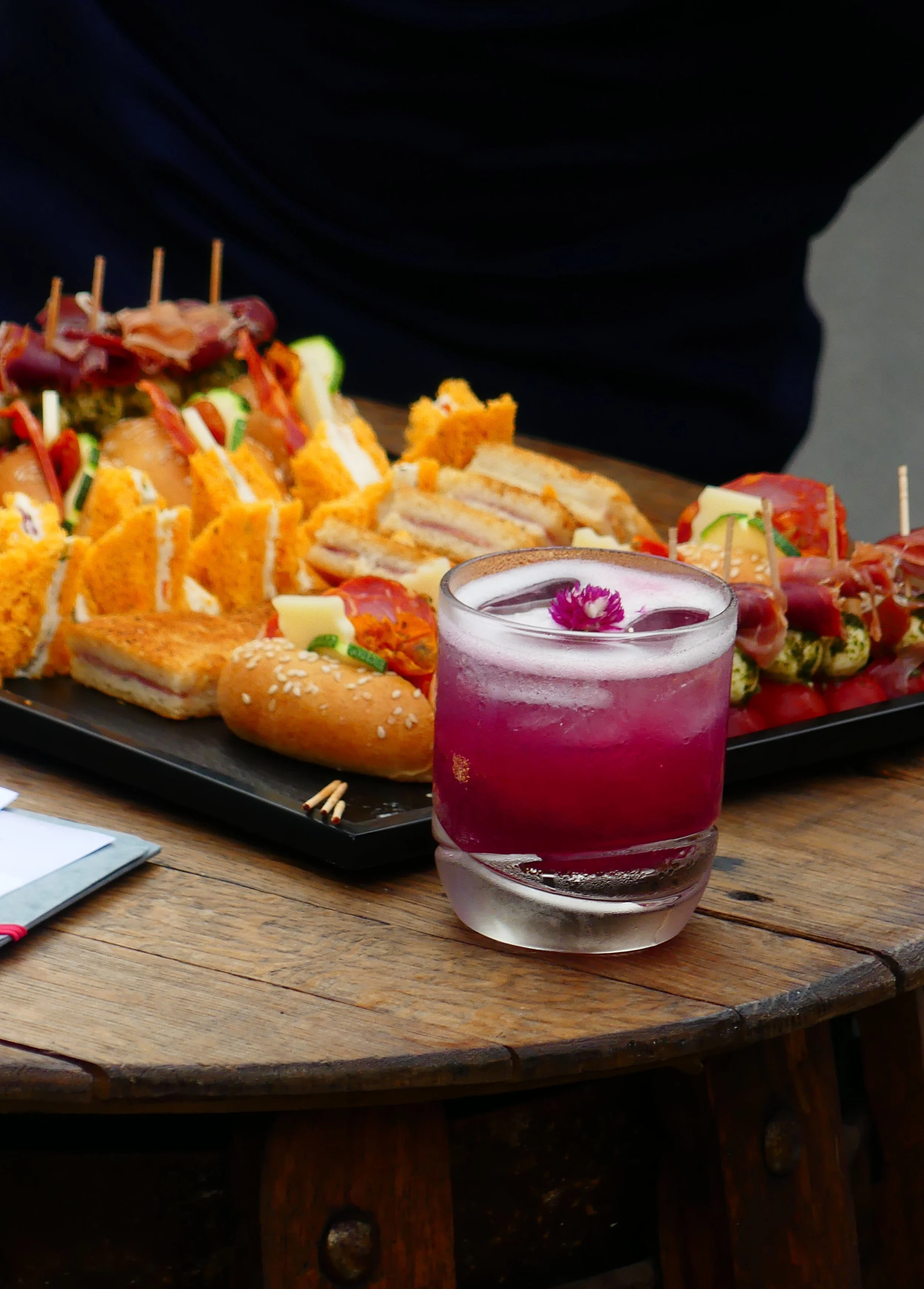 Plateau de amuse-gueules avec sandwichs, cake, et un verre de boisson violette avec glaçons et fleur