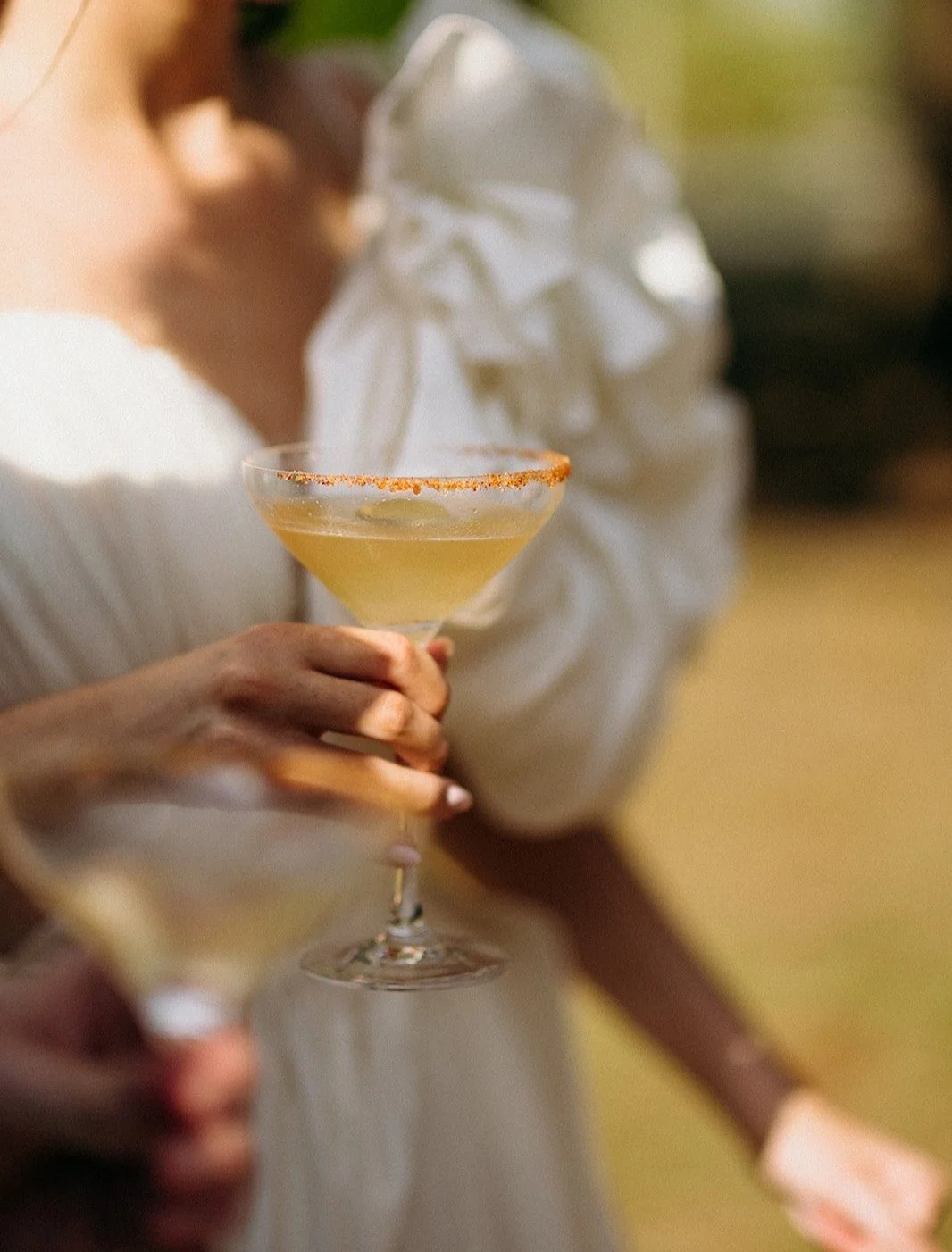 Une personne tient un verre de cocktail jaune avec un rebord épicé, lors d'une célébration ou un rassemblement social.