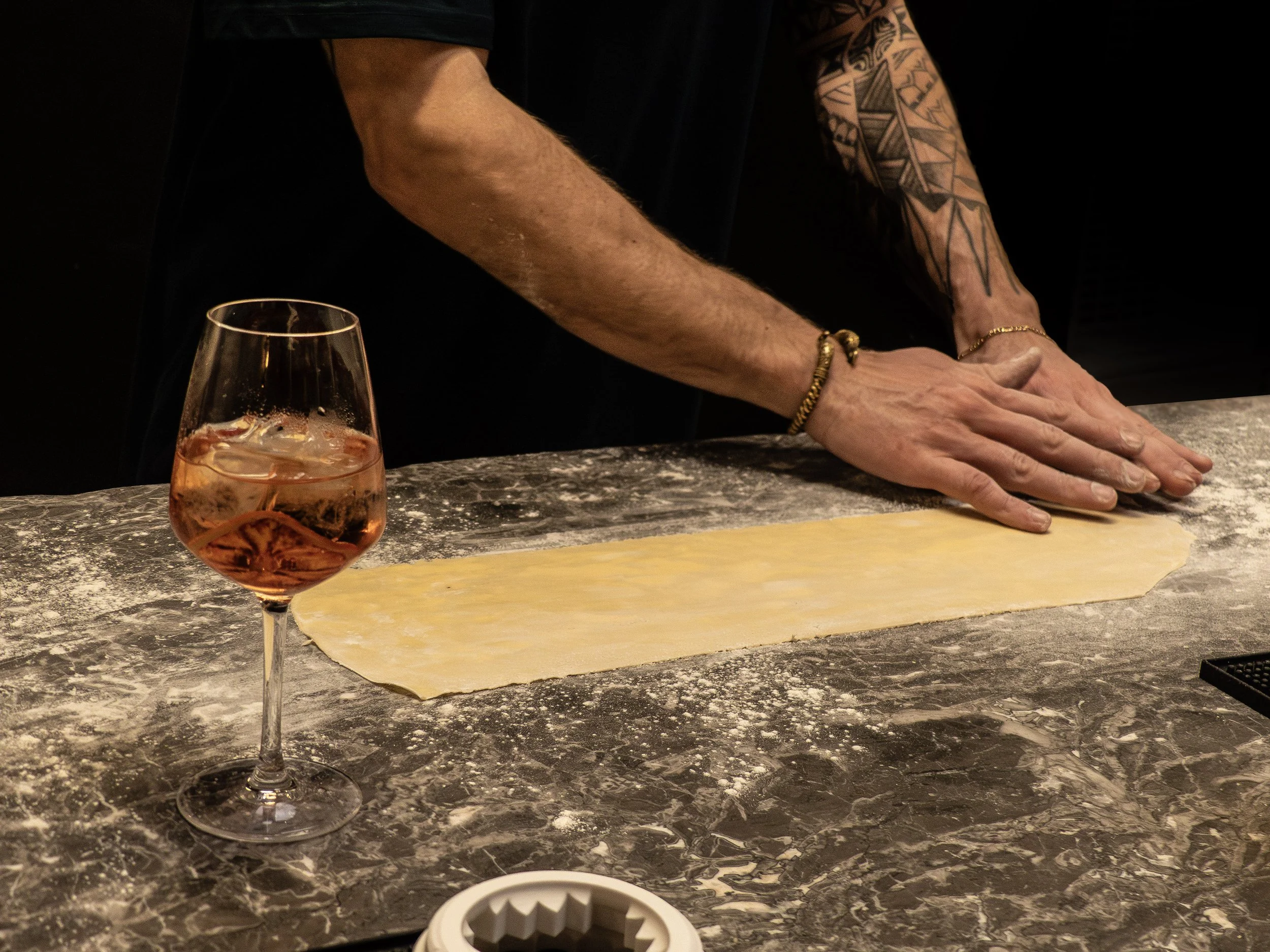 Personne en train de étaler de la pâte à pizza sur un plan de travail en marbre, avec un verre de rosé à proximité.