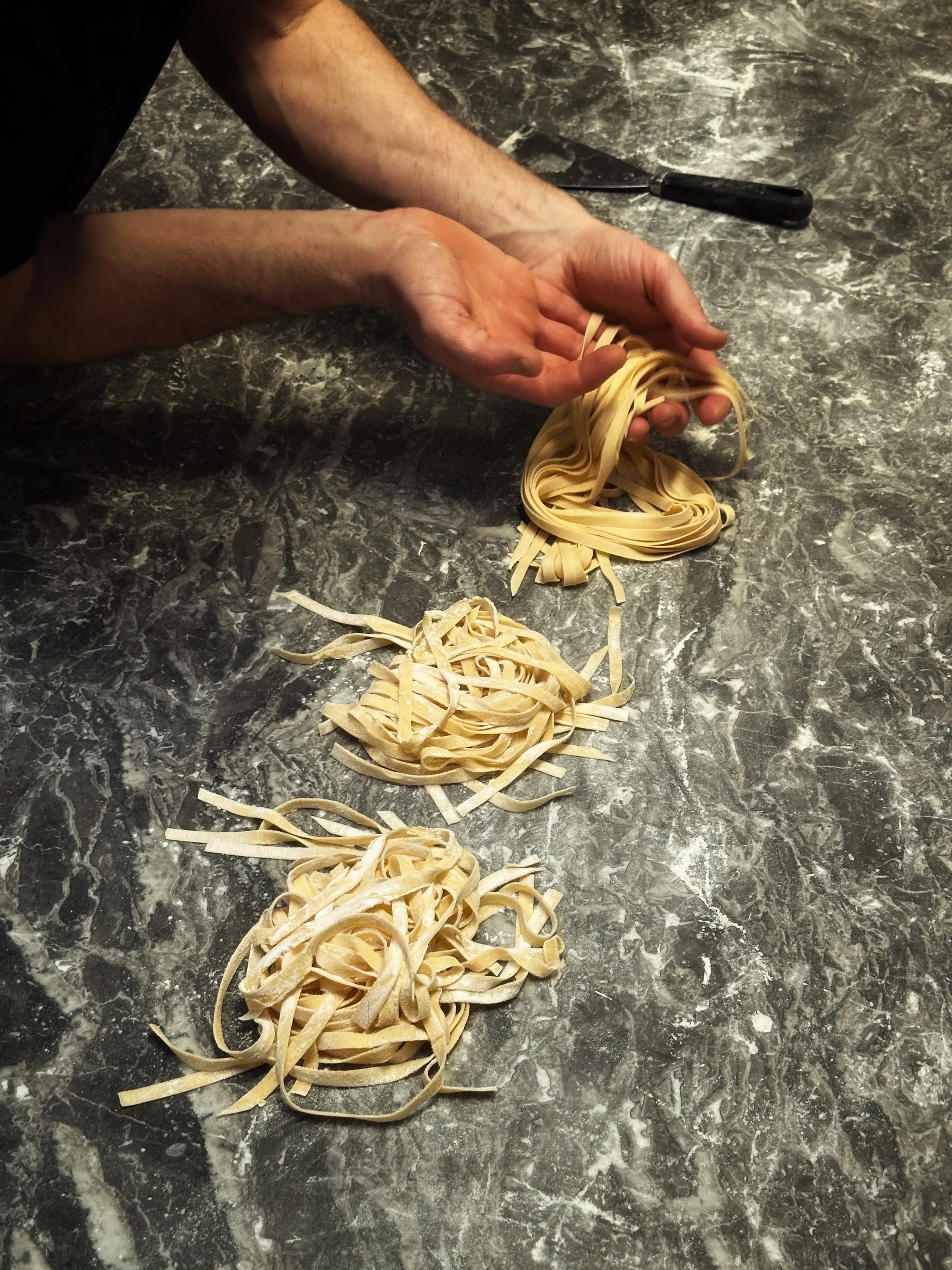 Personnes préparant des pâtes faites maison sur un plan de travail en marbre.