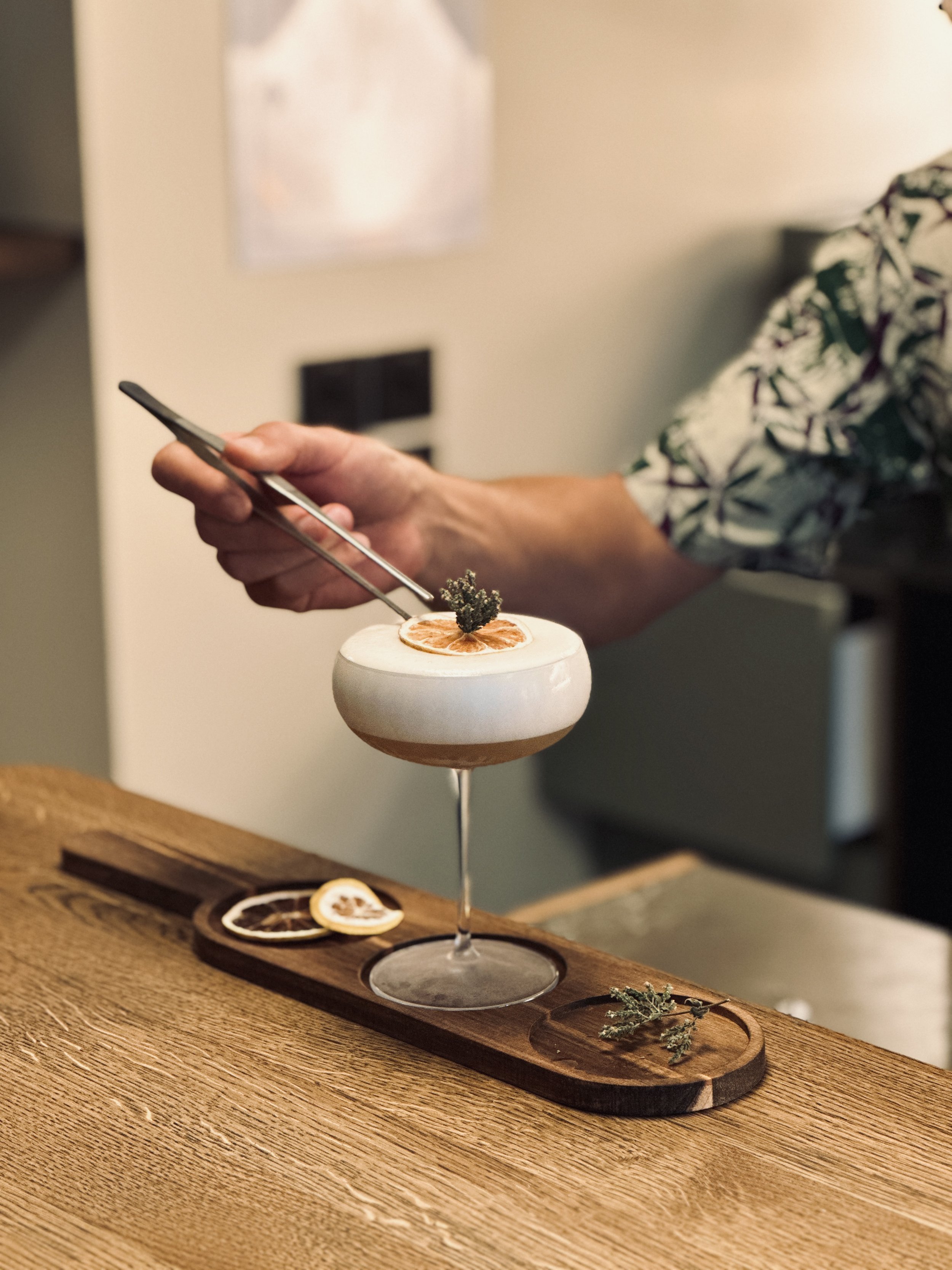 Un cocktail ornée d'une tranche d'orange séchée et d'une branche de thym, placé sur une planche en bois avec des tranches d'orange séchée à côté.