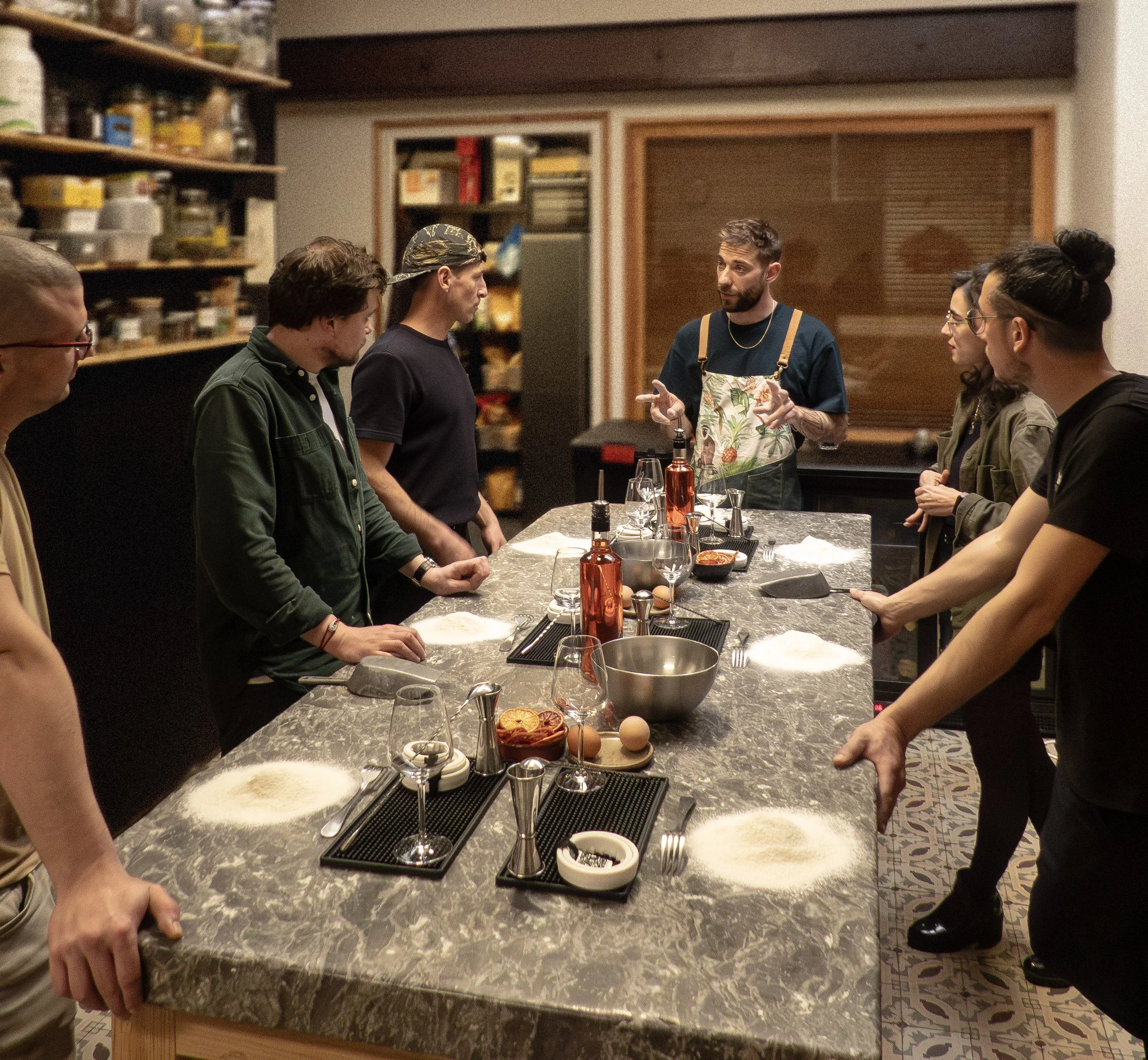 Un groupe de personnes en cuisine, écoutant un chef expliquer des techniques culinaires autour d'une grande table de préparation