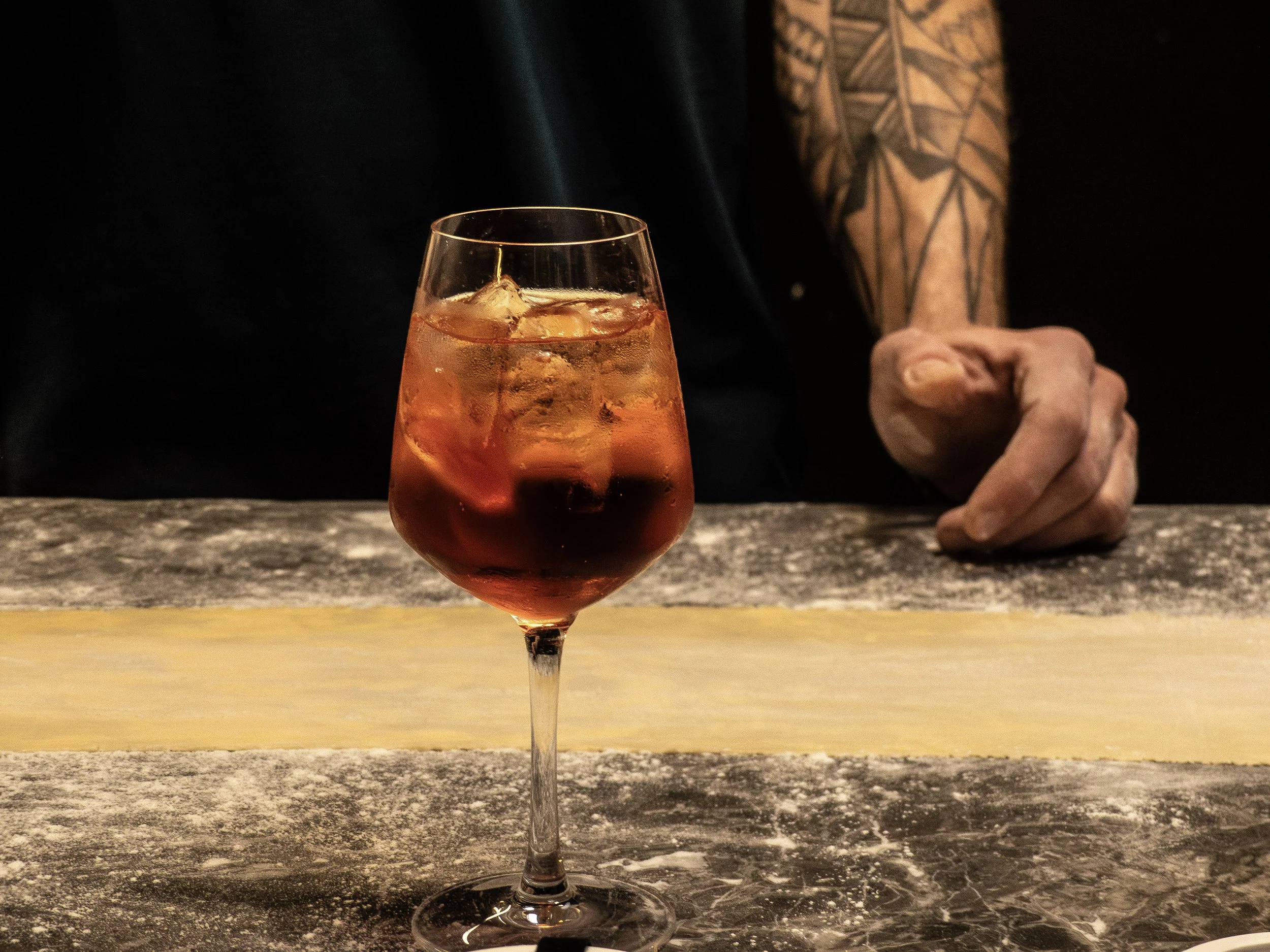 Verre à vin rosé avec glaçons sur un bar en bois, arrière-plan d'un bras d'homme avec tatouages.