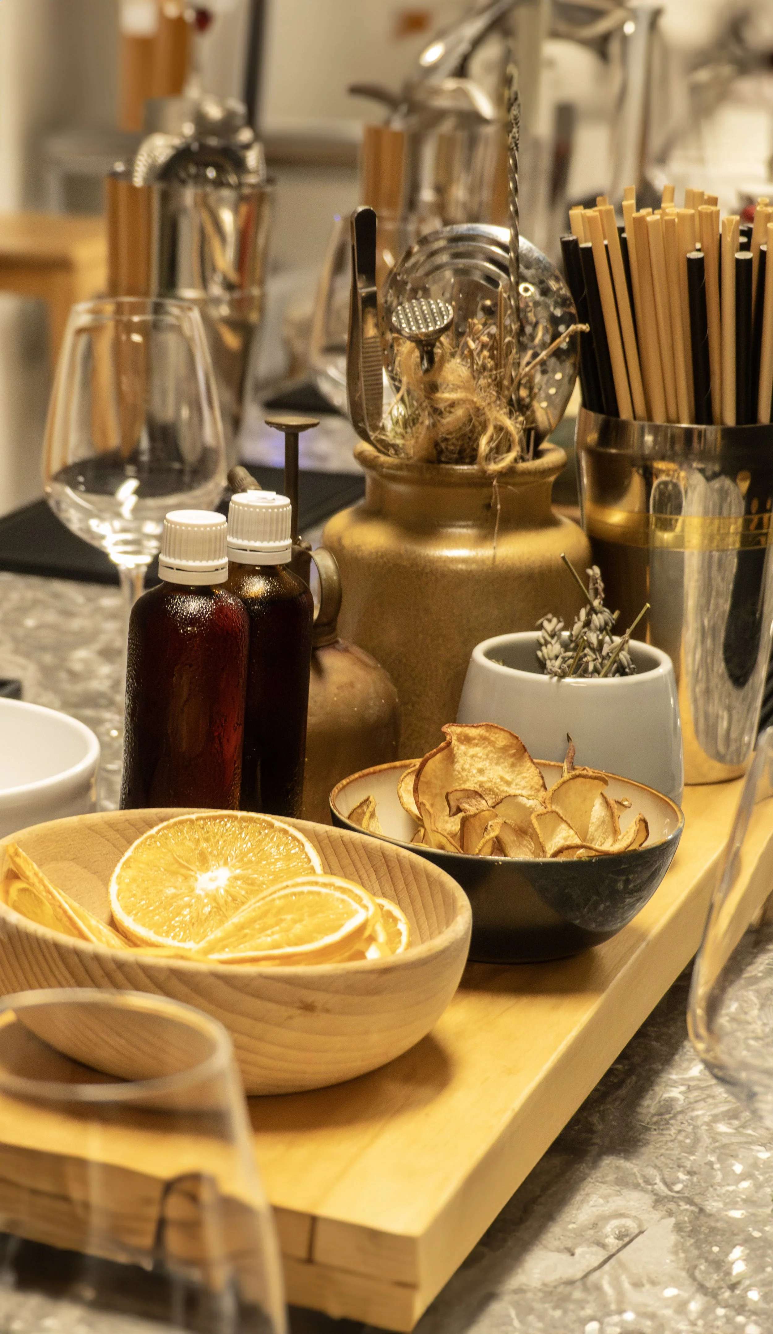 Une planche en bois avec des tranches d'orange, des bols contenant des chips de pomme séchée, et divers ustensiles et accessoires de cuisine sur la table.