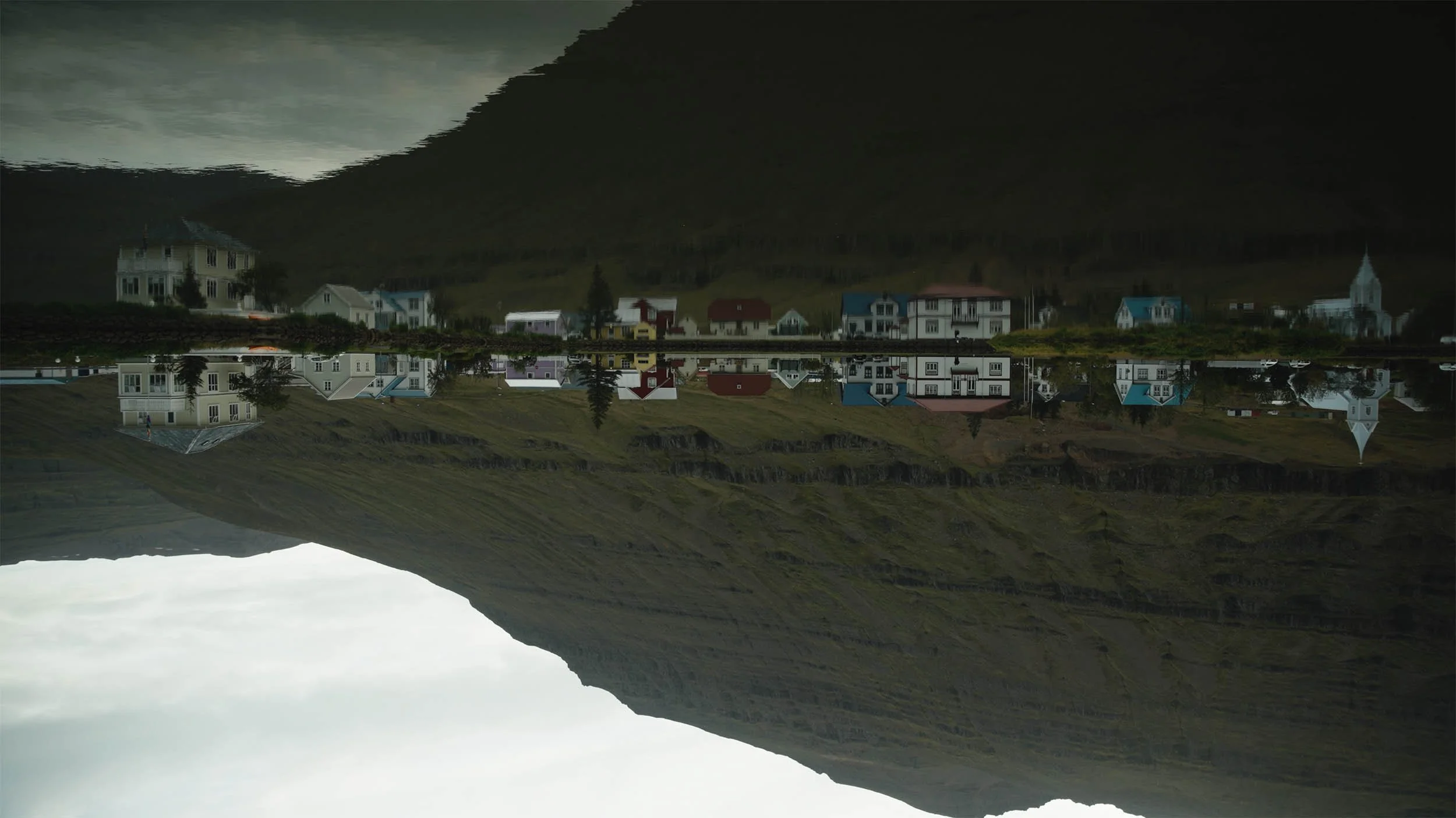 Une image inversée montrant des maisons colorées au bord d'un lac, avec une montagne en arrière-plan, et le reflet des maisons et de la montagne dans l'eau.