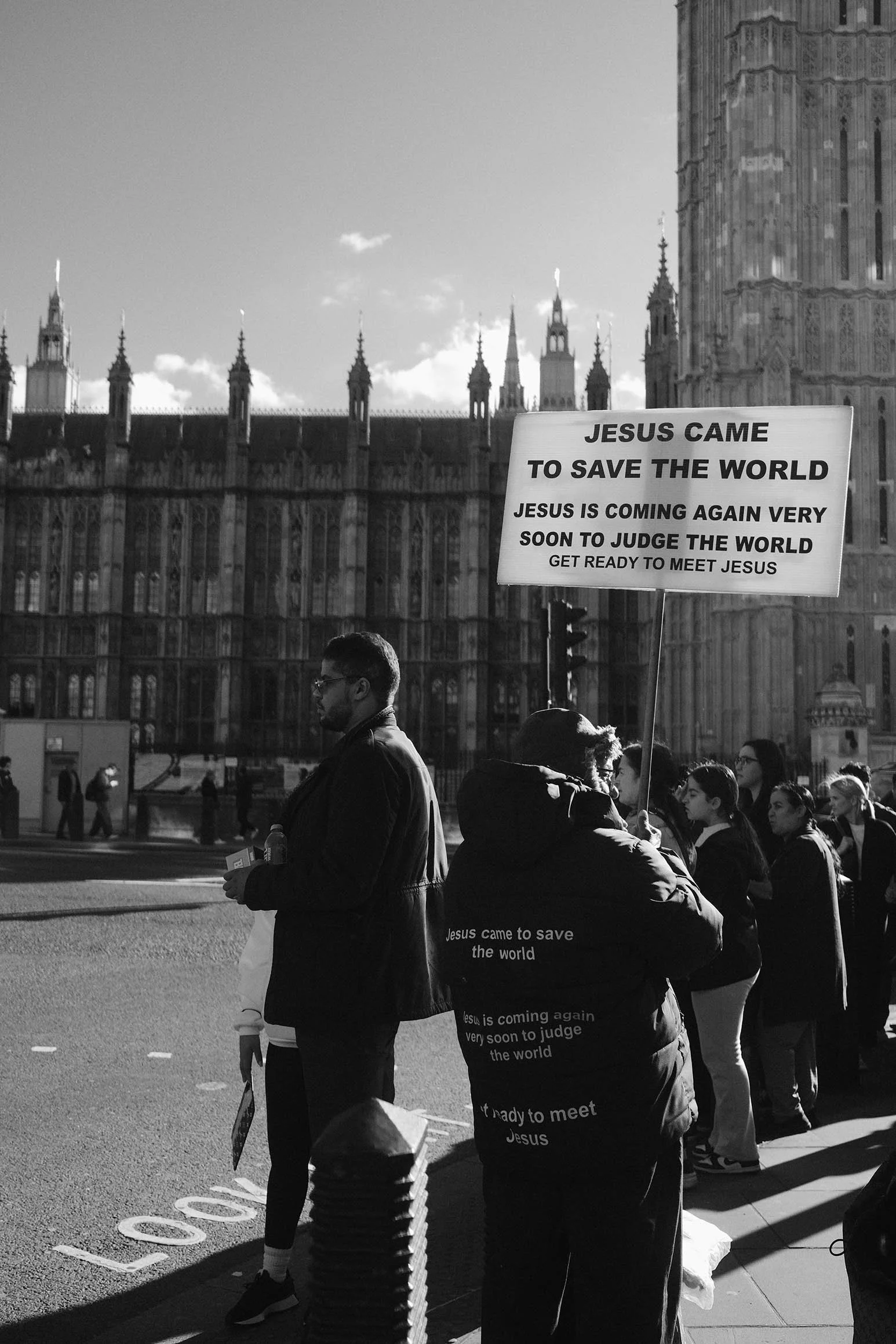 Groupe de personnes en file d'attente devant le Palais de Westminster à Londres, avec un panneau qui annonce le retour de Jésus pour juger le monde.
