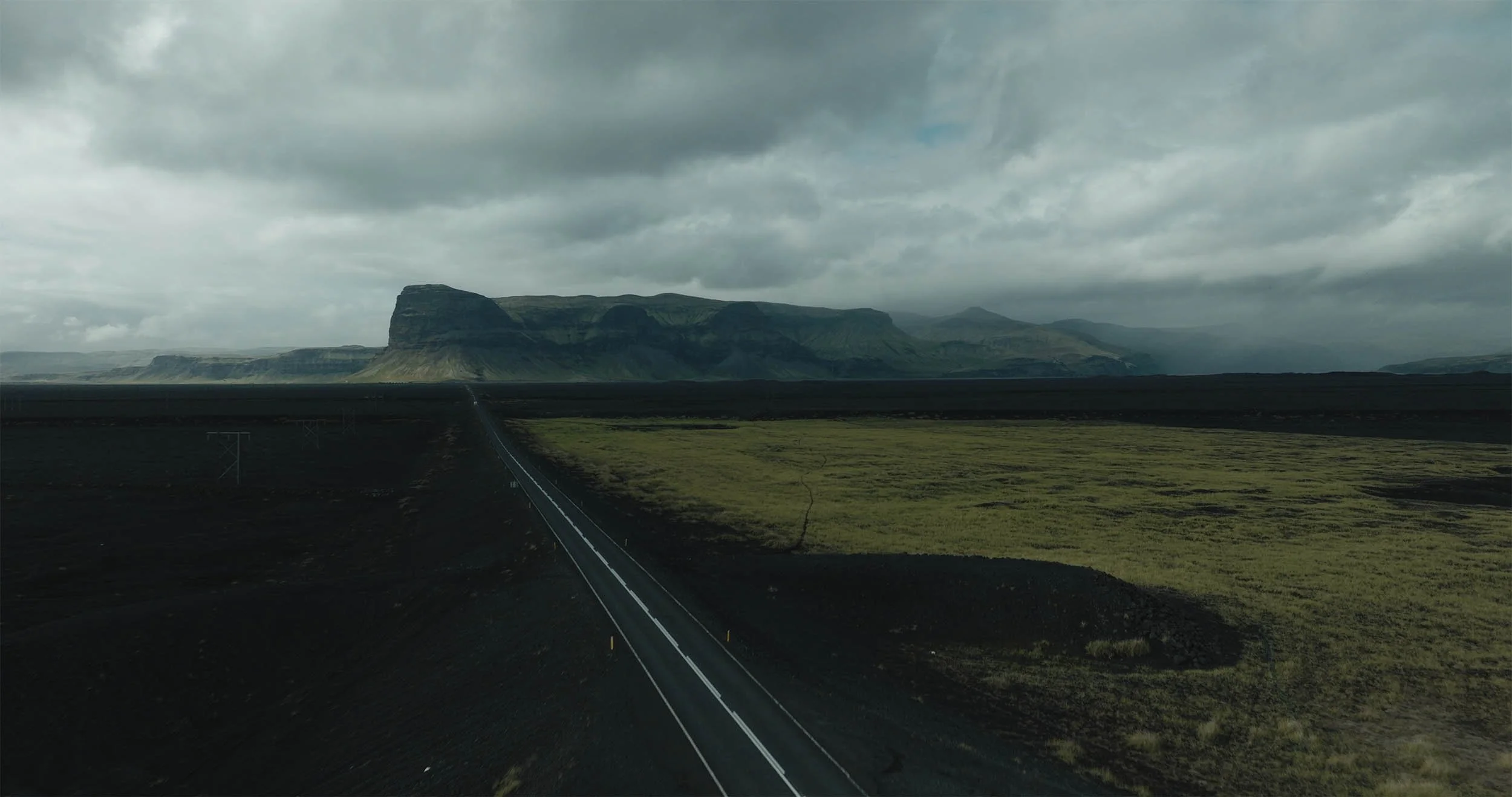 Une route s'étend à travers un paysage désertique avec des montagnes au loin, sous un ciel nuageux.