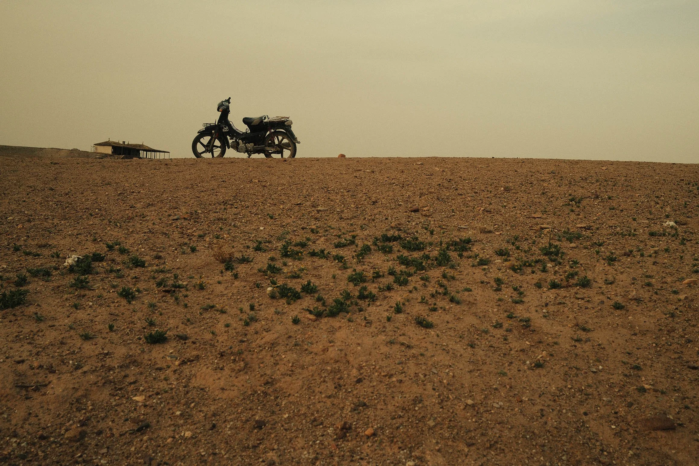 Une moto stationnée sur une colline désertique avec un ciel jaune au crépuscule ou à l'aube.
