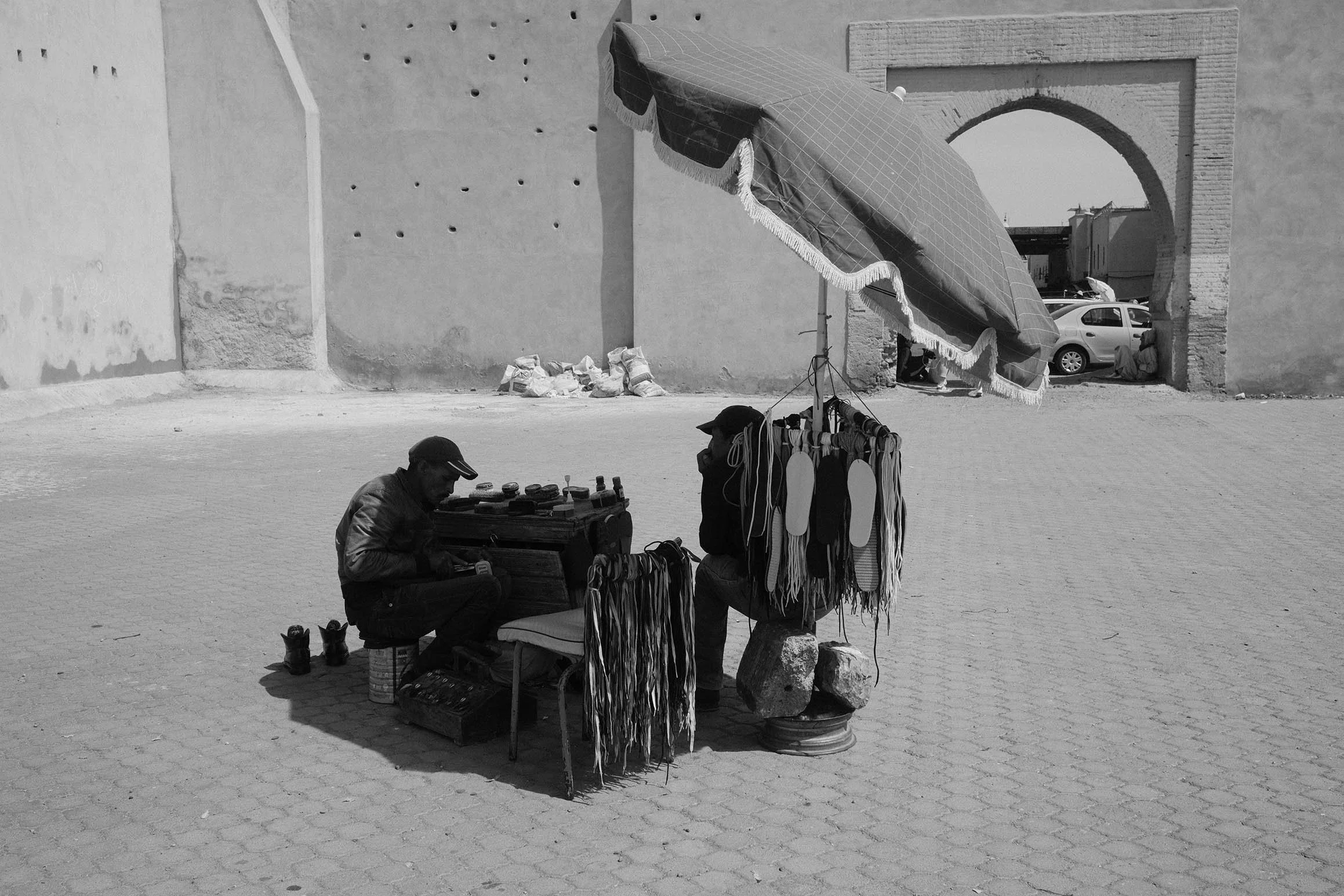 Vendeur ambulant avec des sandales, un parapluie et des vêtements suspendus, en plein air dans une ville, en noir et blanc.