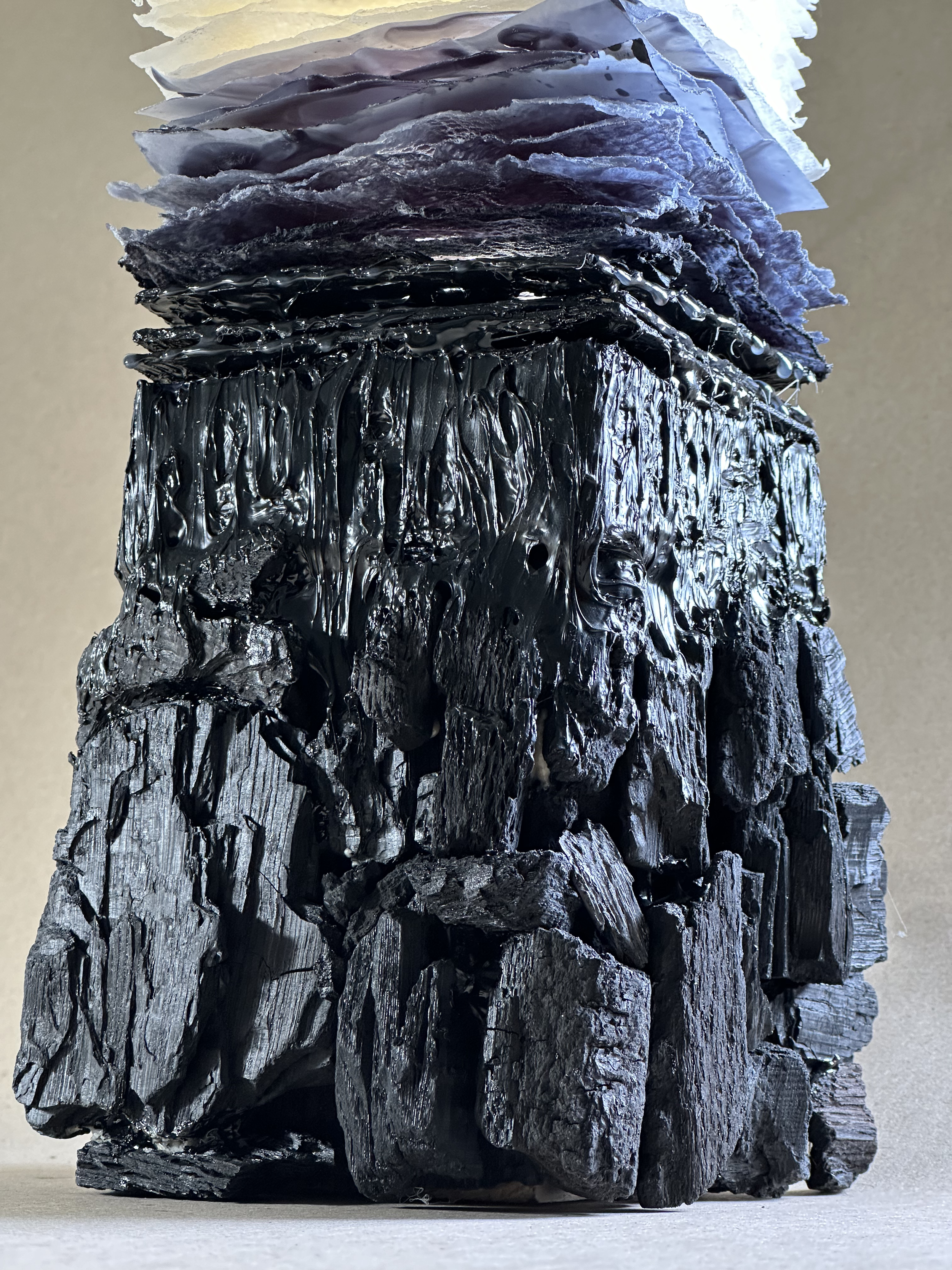 Close-up of a large, textured, black, and gray rock formation with layered, jagged edges, placed on a flat surface against a plain background.