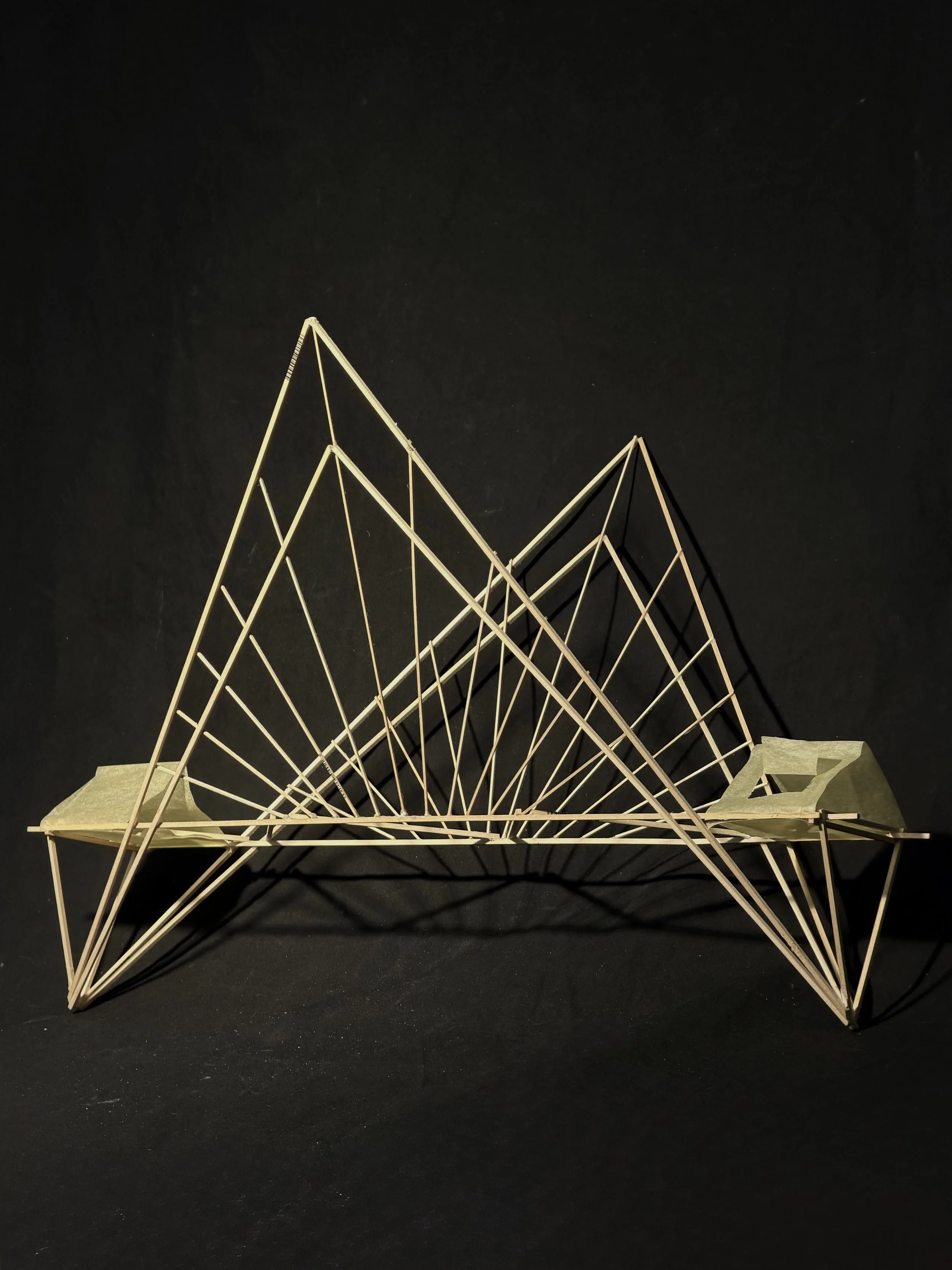 A wooden geometric architectural model with triangular and diamond-shaped frames, set against a black background.