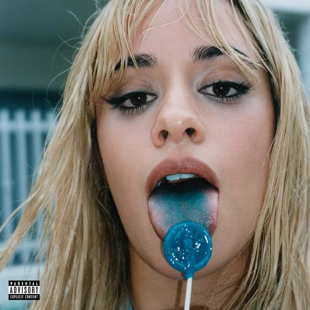 A woman with blonde hair and makeup licking a blue lollipop.