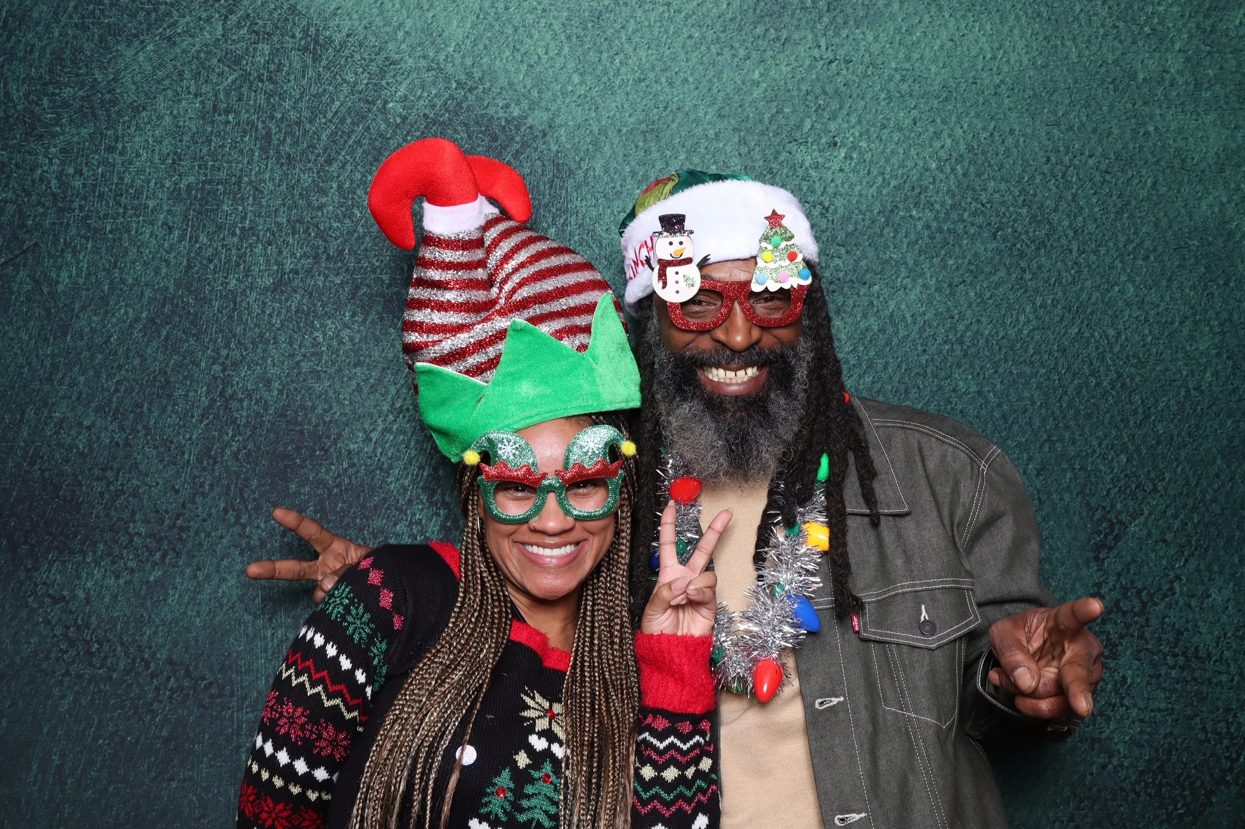 Photo booth setup with a green backdrop, a white photo stand, and a small table with a vase of ornamental grasses.