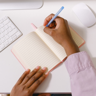 Person writing in an open notebook at a desk