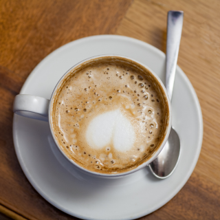 A cup of coffee with foam art on a saucer with a spoon, on a wooden table