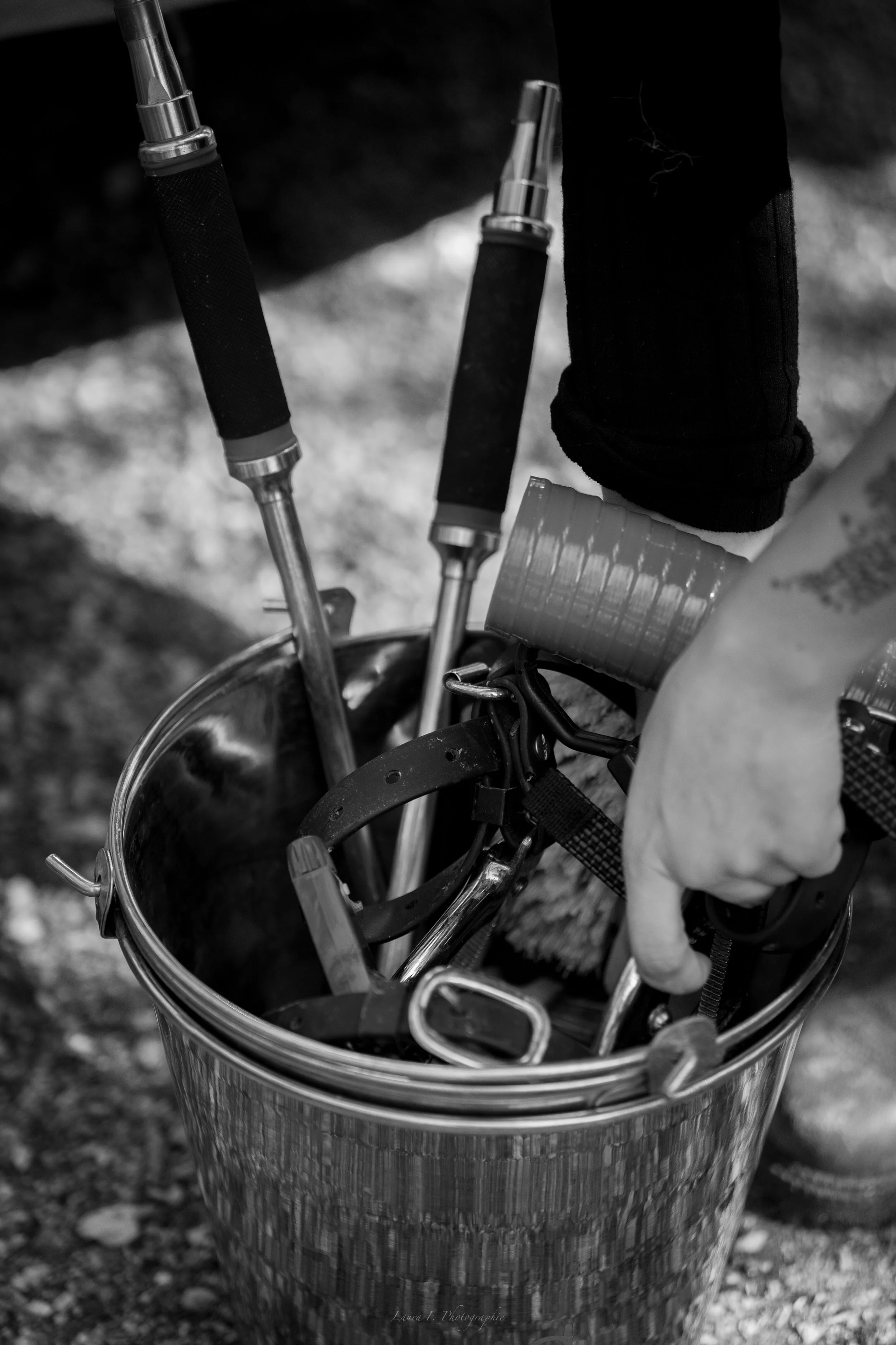 Une main tenant une bouteille en métal dans un seau contenant des équipements d'escalade, avec quelques bâtons ou piolets visibles.