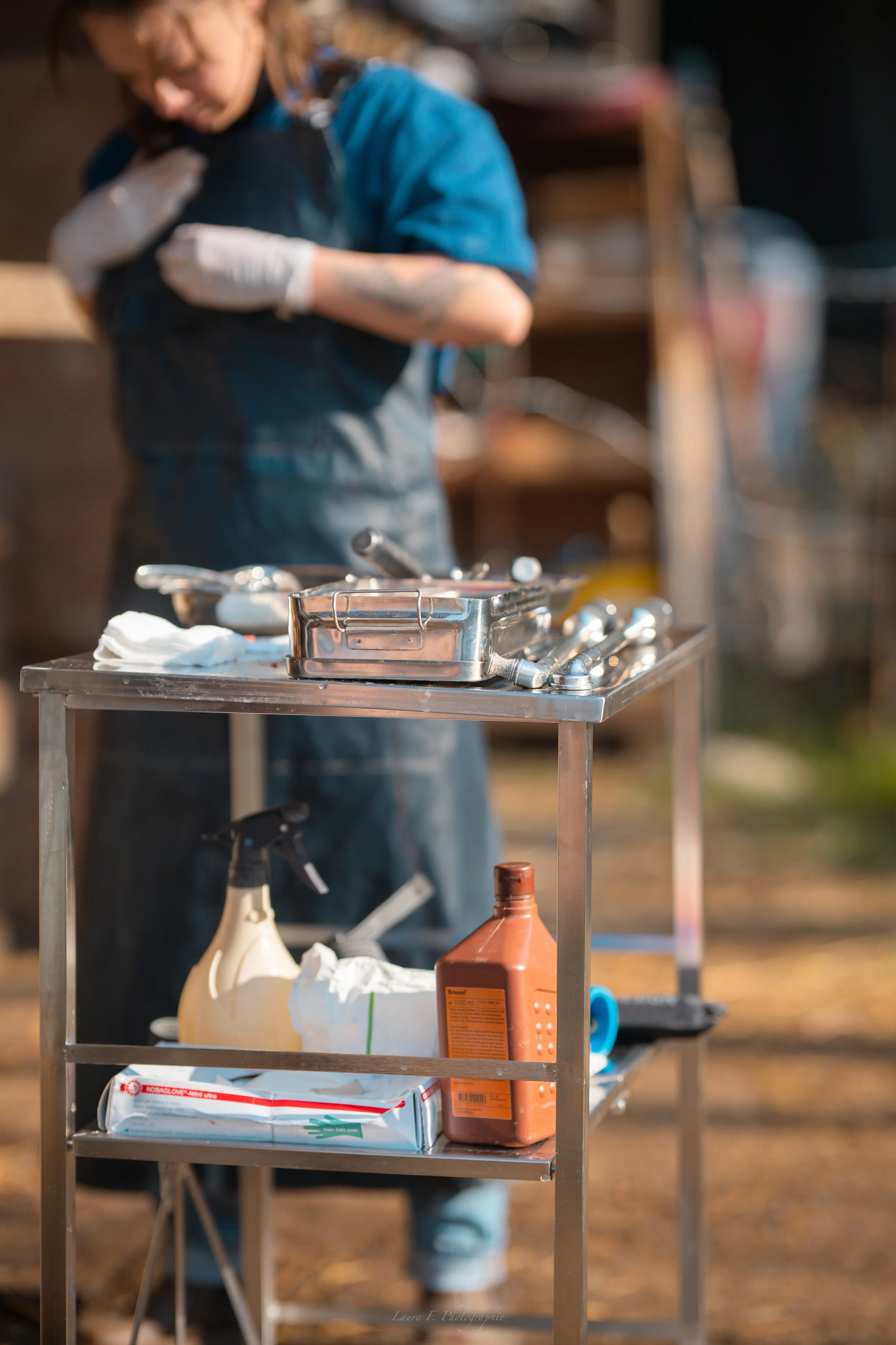 Une personne en blouse de cuisine travaillant à une station de cuisine en extérieur, avec des ustensiles et produits de cuisine sur une table en métal.