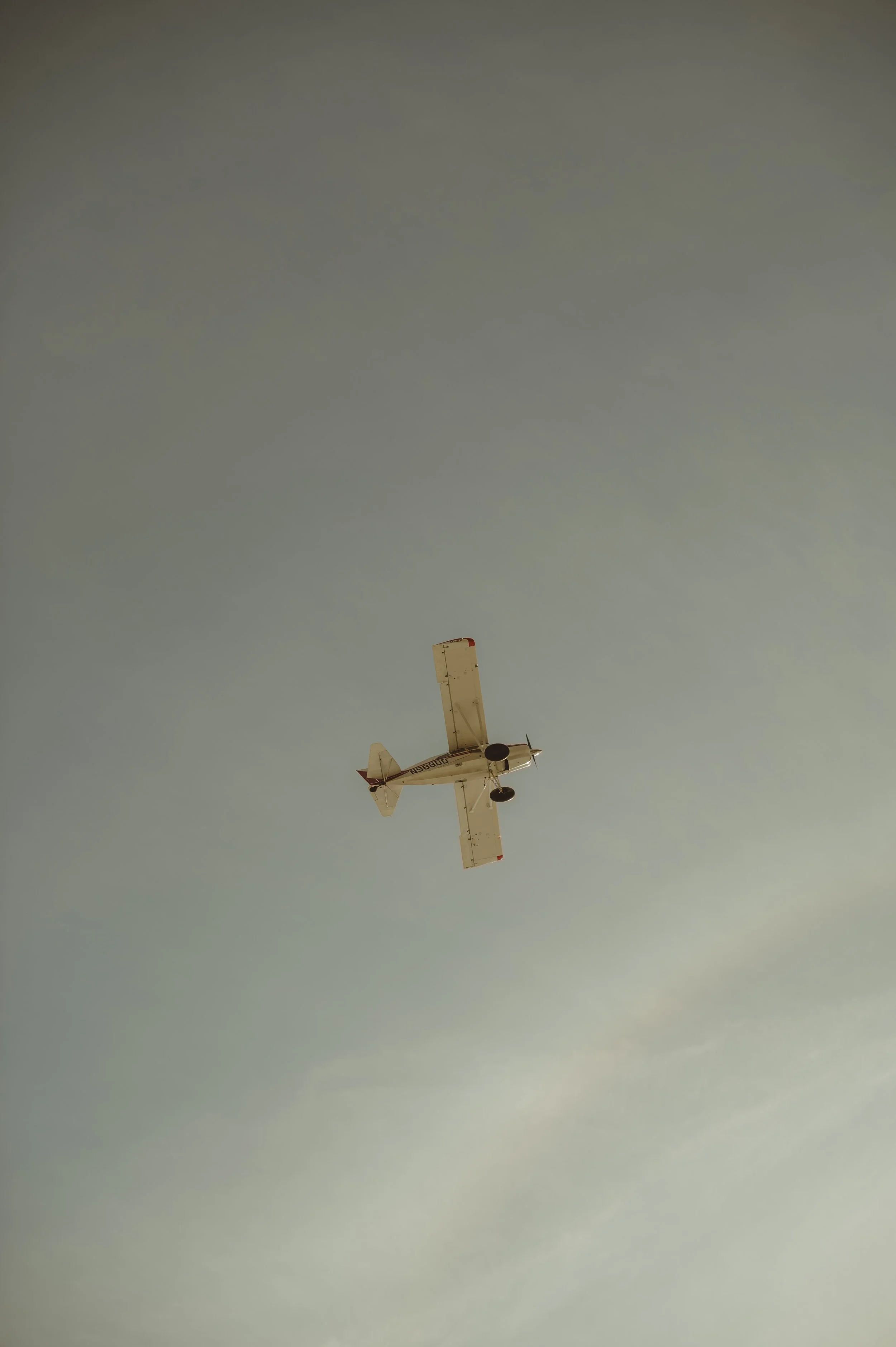 Small white airplane flying in a clear bluish sky with a few clouds.