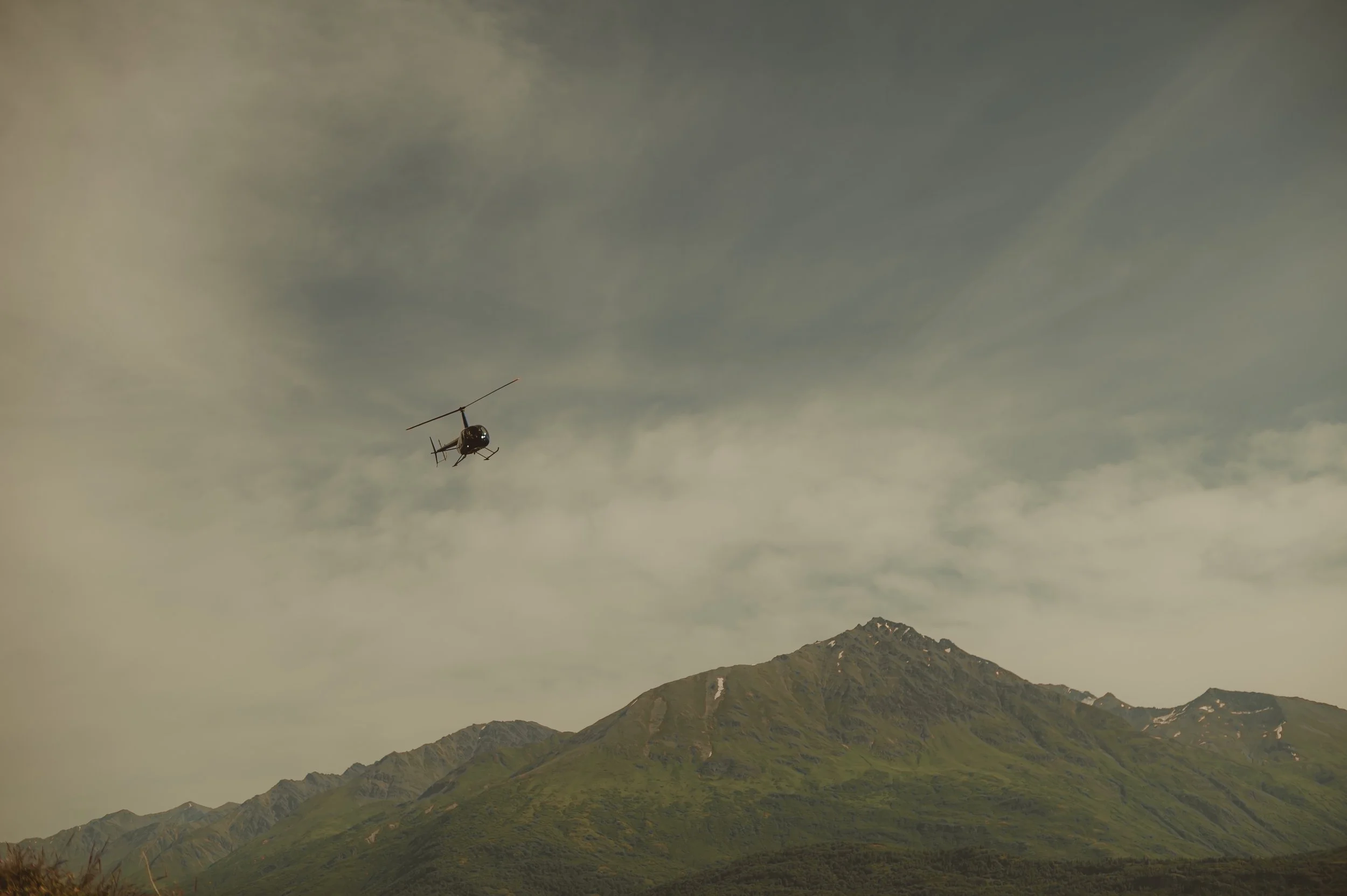 A helicopter flying over a mountainous landscape with cloudy skies.