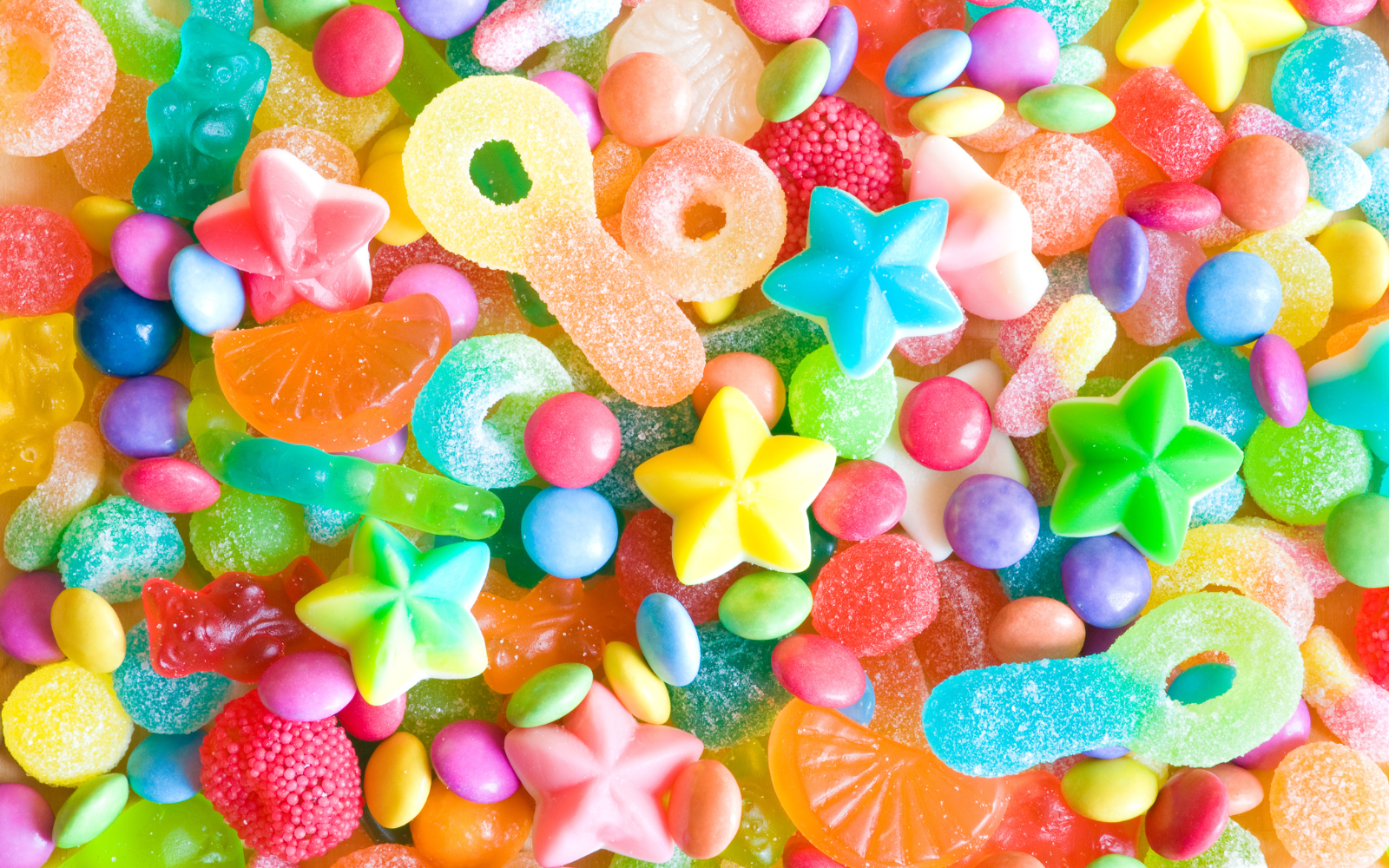 Colorful assortment of assorted gummy candies and jelly beans in various shapes such as stars, flowers, fruit slices, and circular pieces.