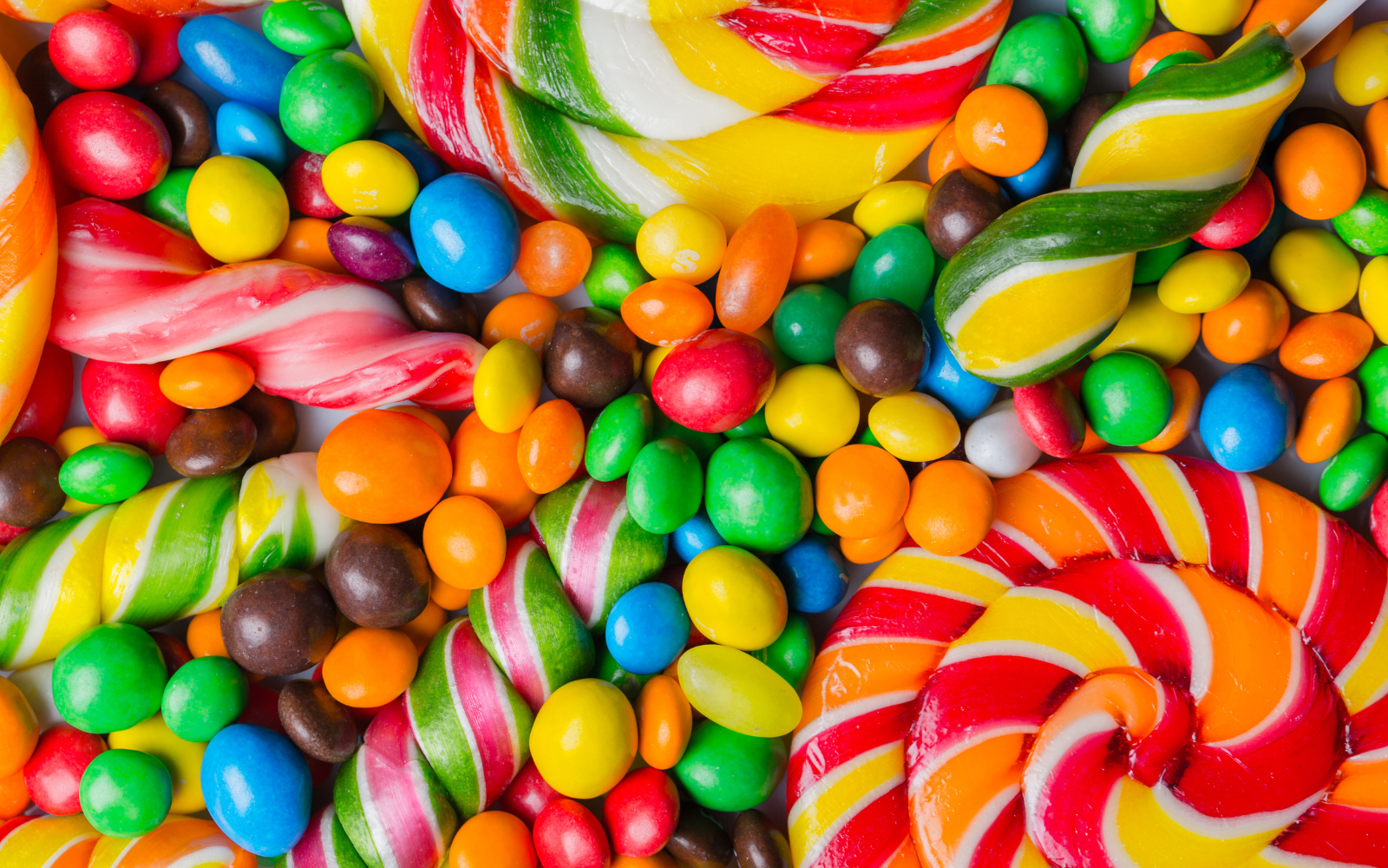 A variety of colorful candies including striped lollipops, gum balls, jelly beans, and twisted candies in bright colors.