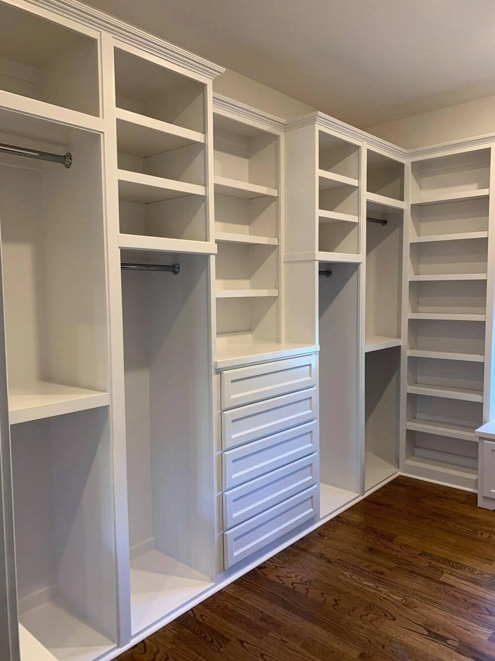 Empty white custom closet with shelves, drawers, and hanging rods, with hardwood floor.