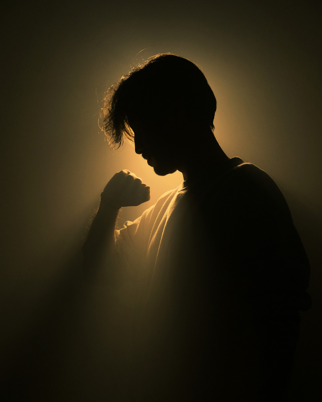 Silhouette of a man with tousled hair, making a fist and showing a confident pose, backlit with warm light.
