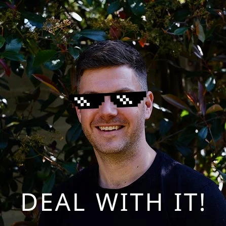 Person wearing pixelated sunglasses with 'Deal With It' text, standing in front of leafy background.