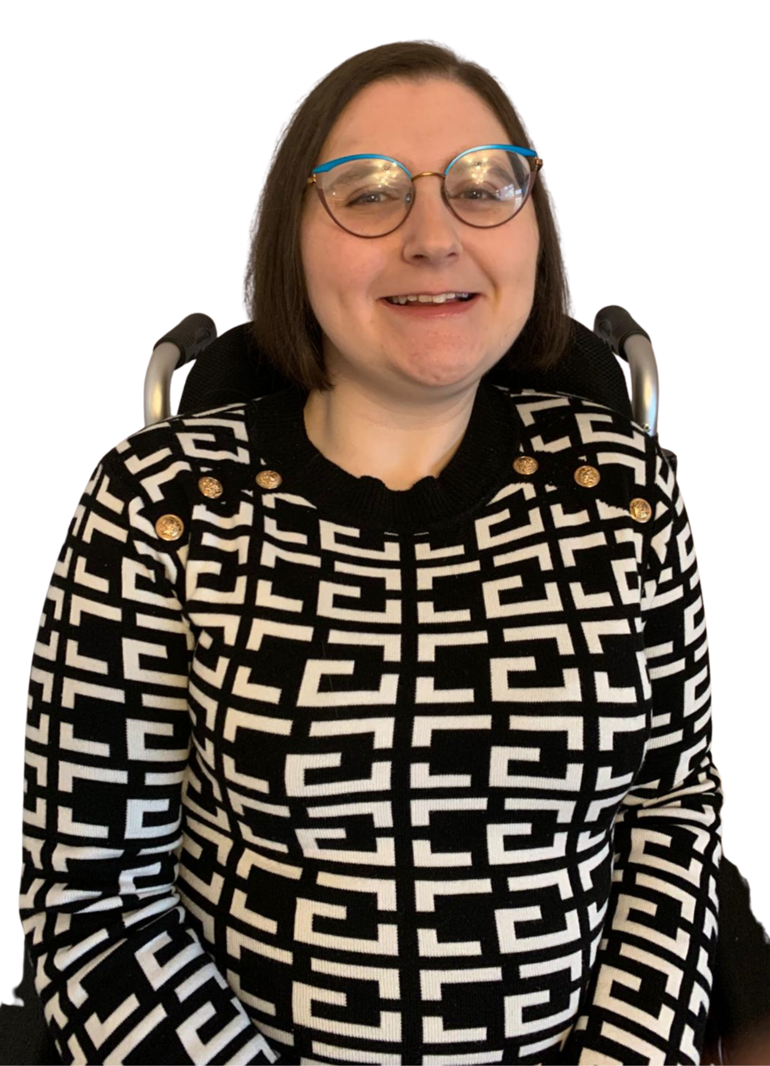 A person with shoulder-length dark hair wearing glasses and a black and white patterned sweater with gold buttons, sitting in a wheelchair smiling.