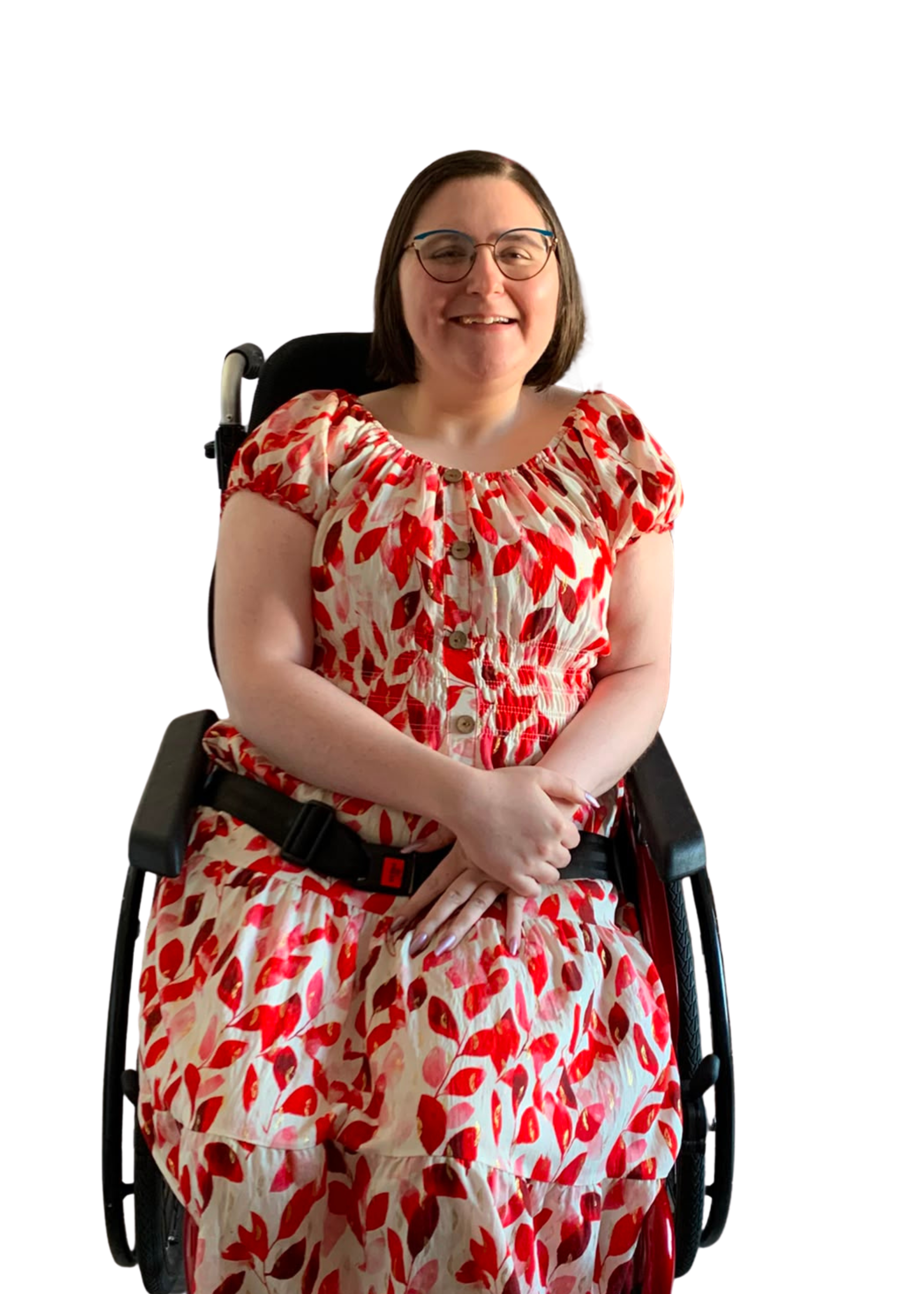 A woman with short brown hair, glasses, and light skin sitting in a wheelchair, smiling, wearing a dress with a red and beige leaf pattern.