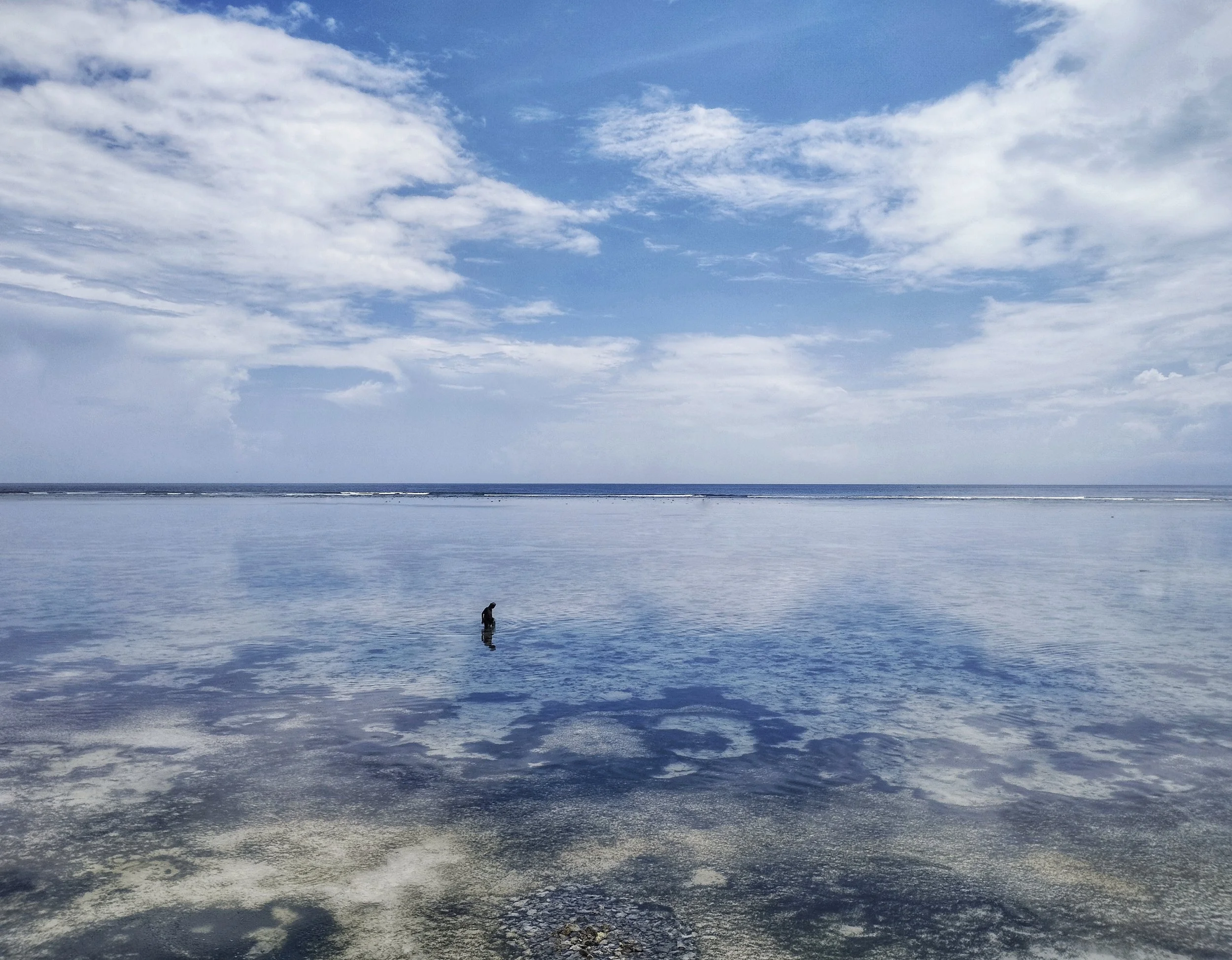 Small distant figure on a vast tidal flat beneath a large cloud, black and white.