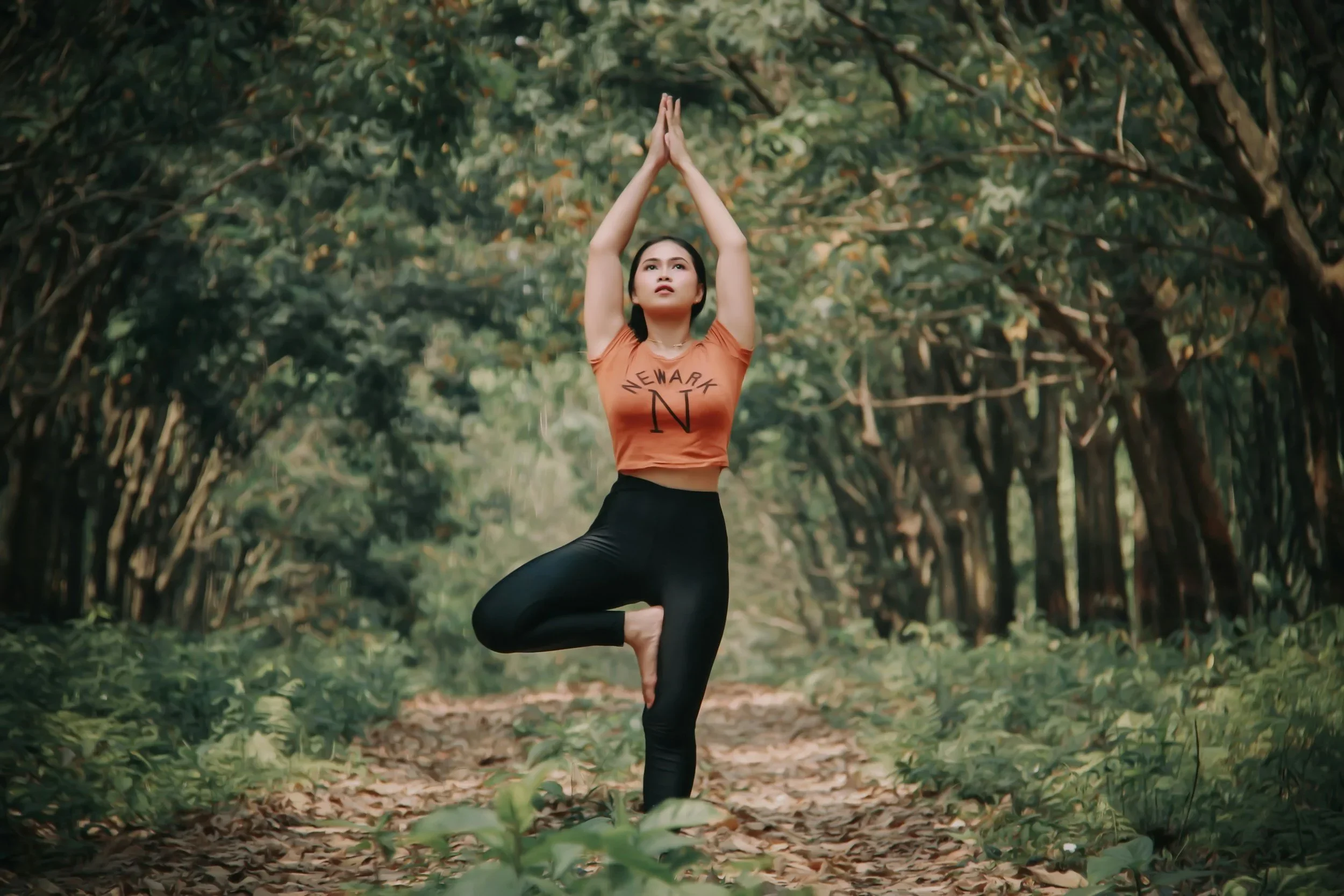 Woman practicing yoga in a peaceful forest, balancing on one foot with hands raised above her head.