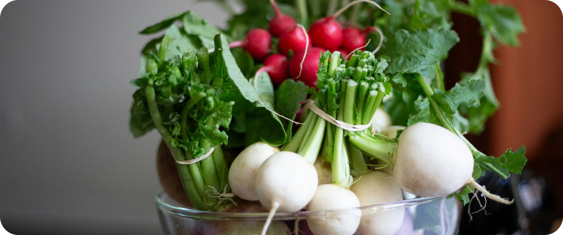 Fresh radishes, turnips, and green leafy vegetables in a glass bowl.