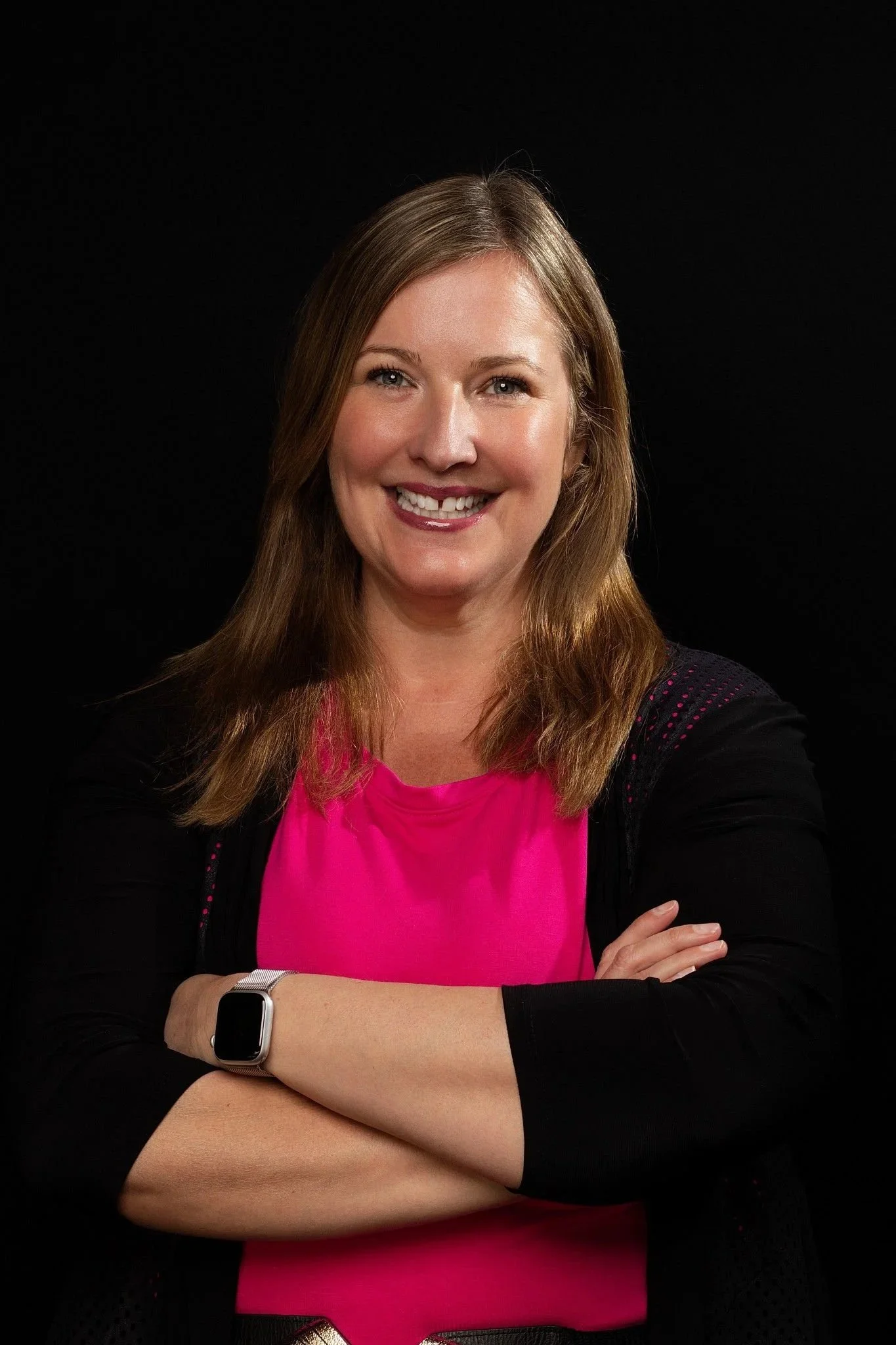 Photo of Tina smiling, pink dress, black sweater, arms crossed