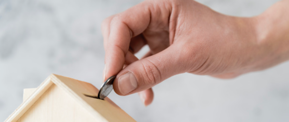 A hand placing a coin into a wooden birdhouse.