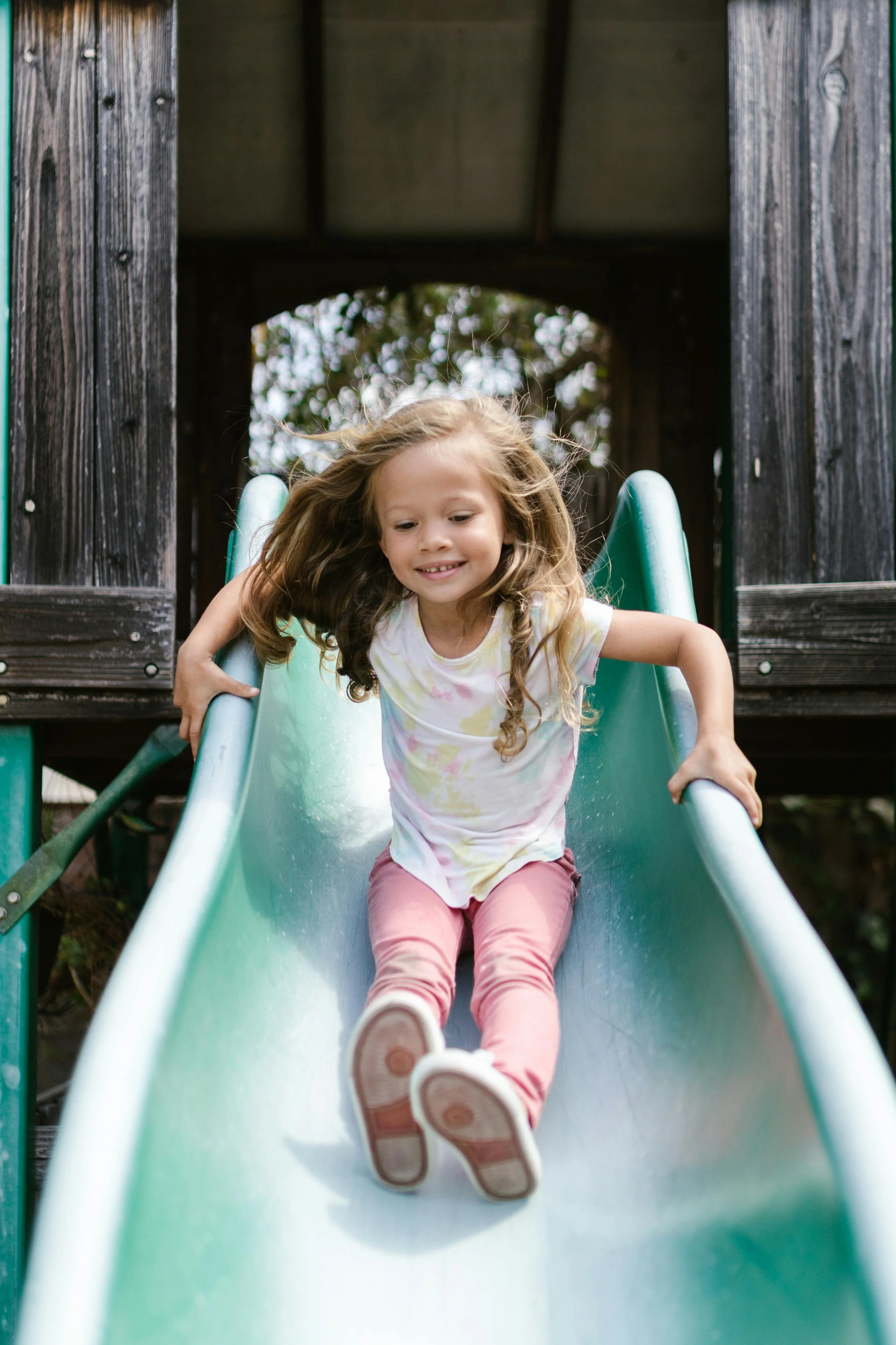 Young girl with long curly hair sliding down a green playground slide.