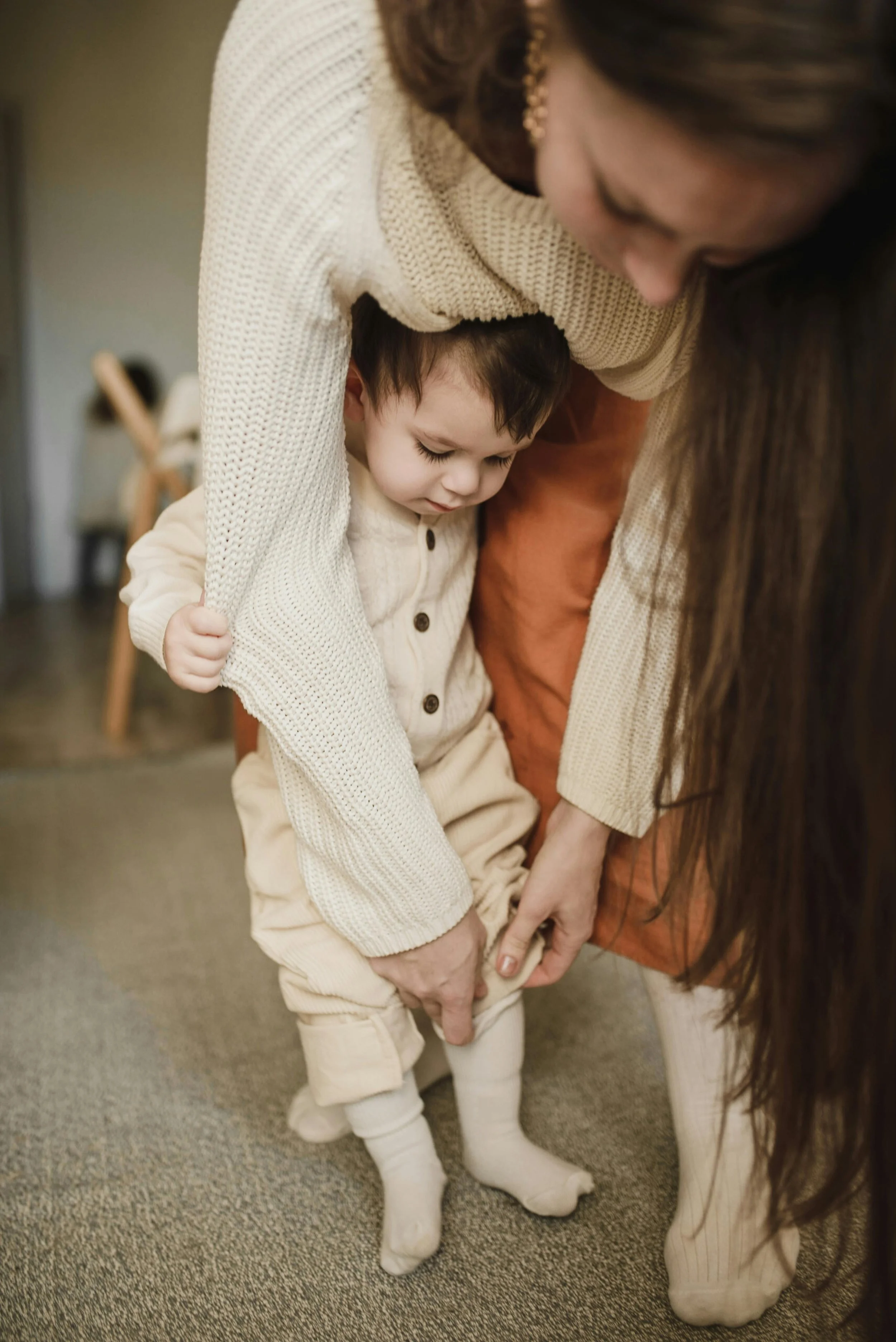 An adult helping a young child put on socks, with both focused on the task.