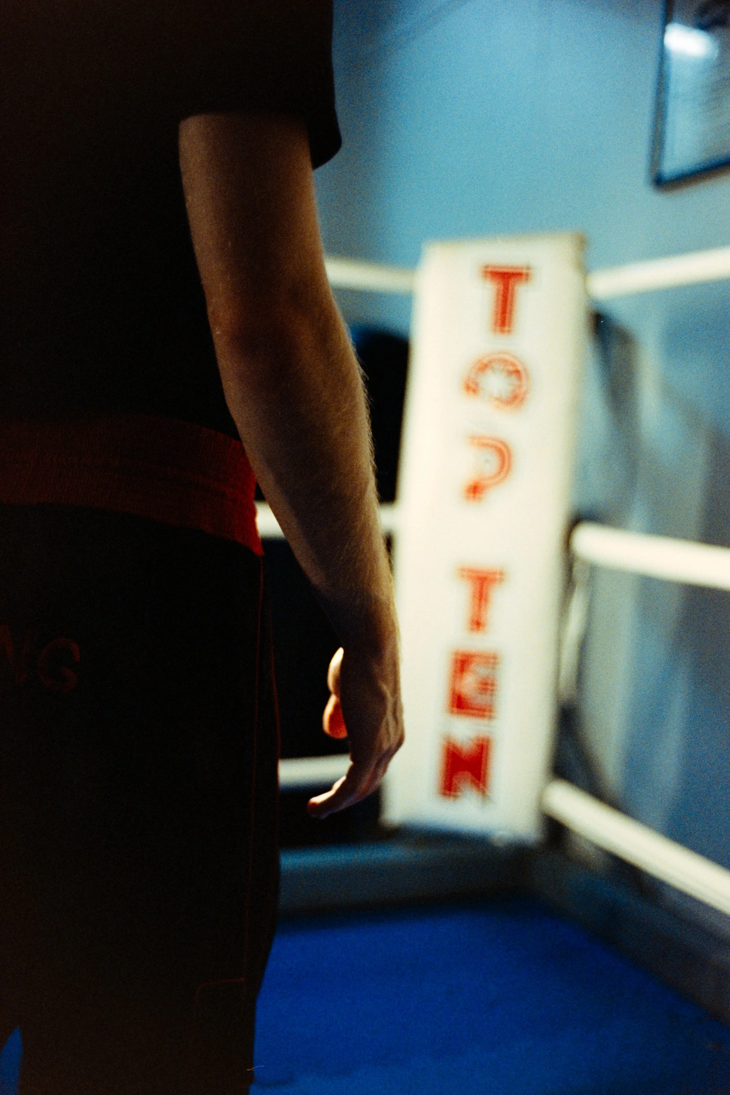 Close-up of a boxer wearing black shorts with red waistband, standing in a boxing ring with a sympathy sign in the background.