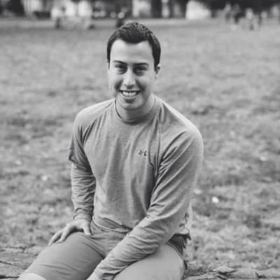 Young man sitting outdoors on grass, smiling, black and white photo.