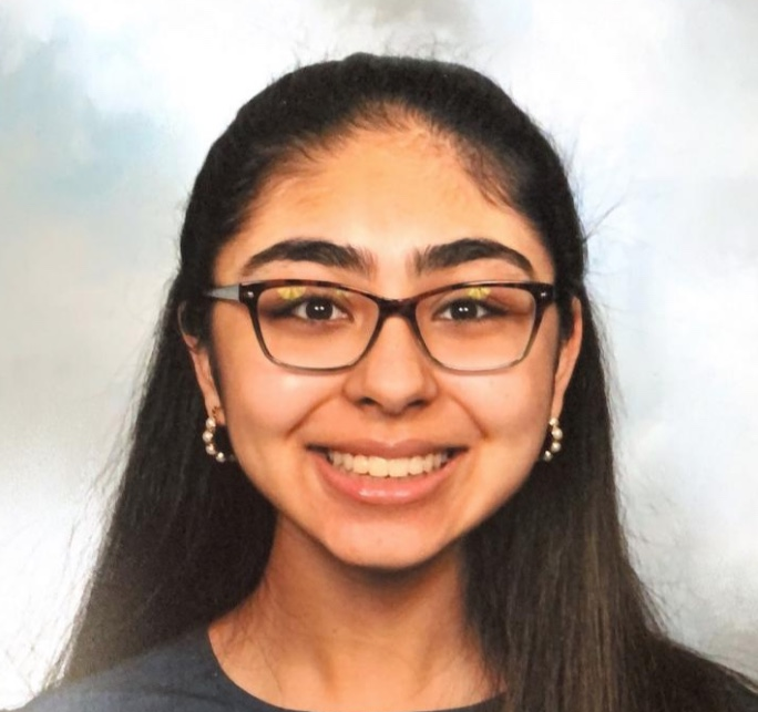 Young woman with long black hair, glasses, and earrings, smiling at the camera.
